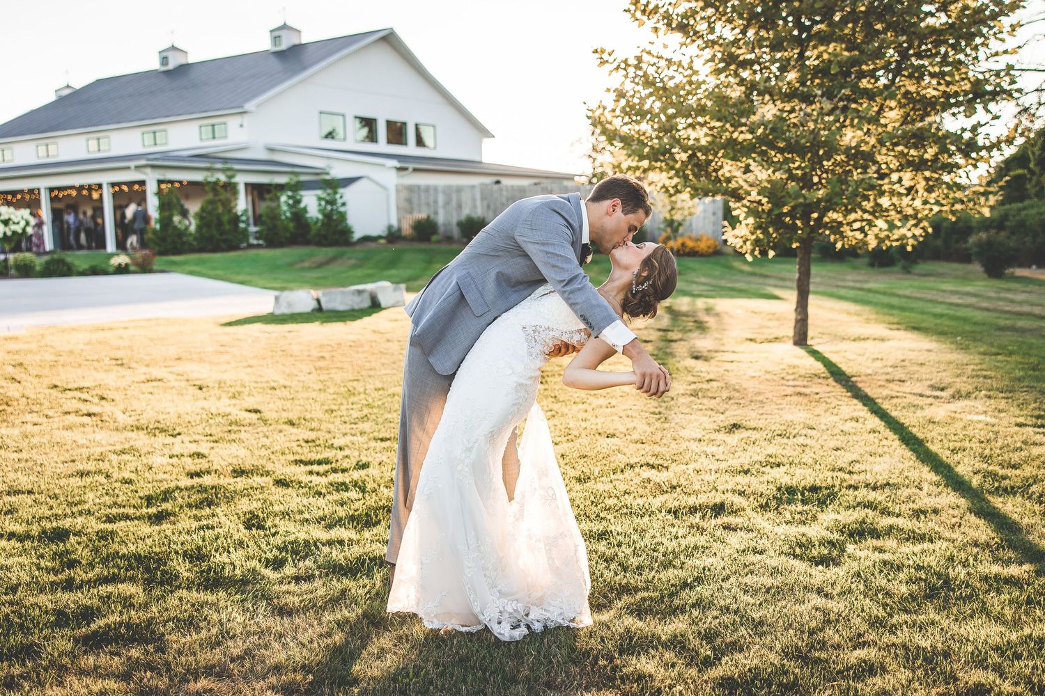 A romantic dip pose on a sunlit lawn with a white house in the background.