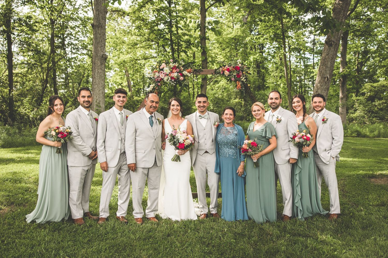 Wedding party in light blue dresses and white suits posed together on grassy hillside.