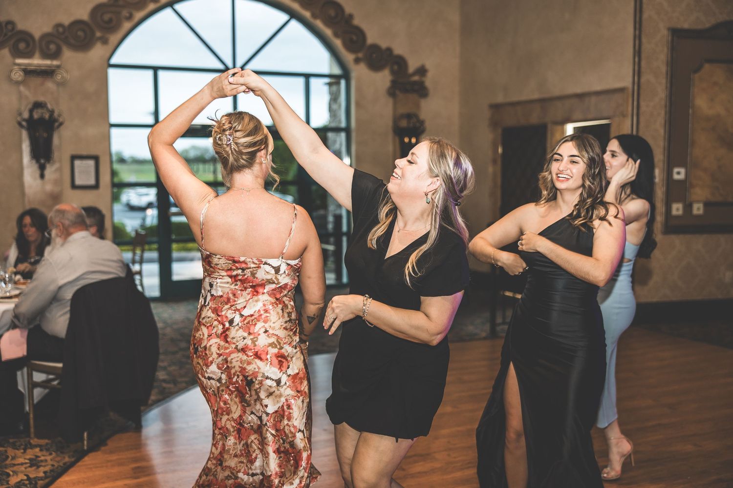 Wedding guests dancing together on a wooden dance floor at a reception venue.