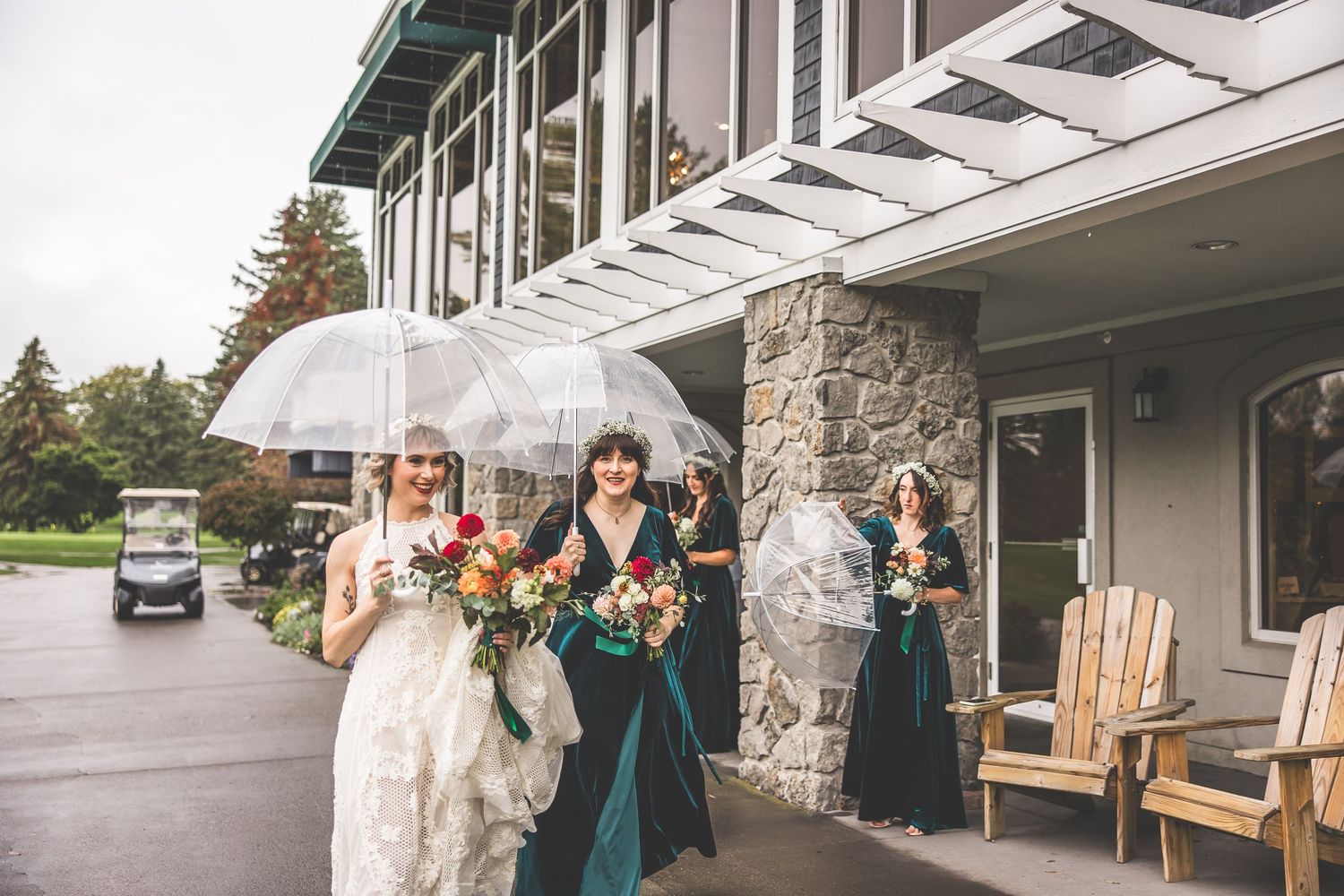 Wedding party members hold clear umbrellas outside a stone building on a rainy day.