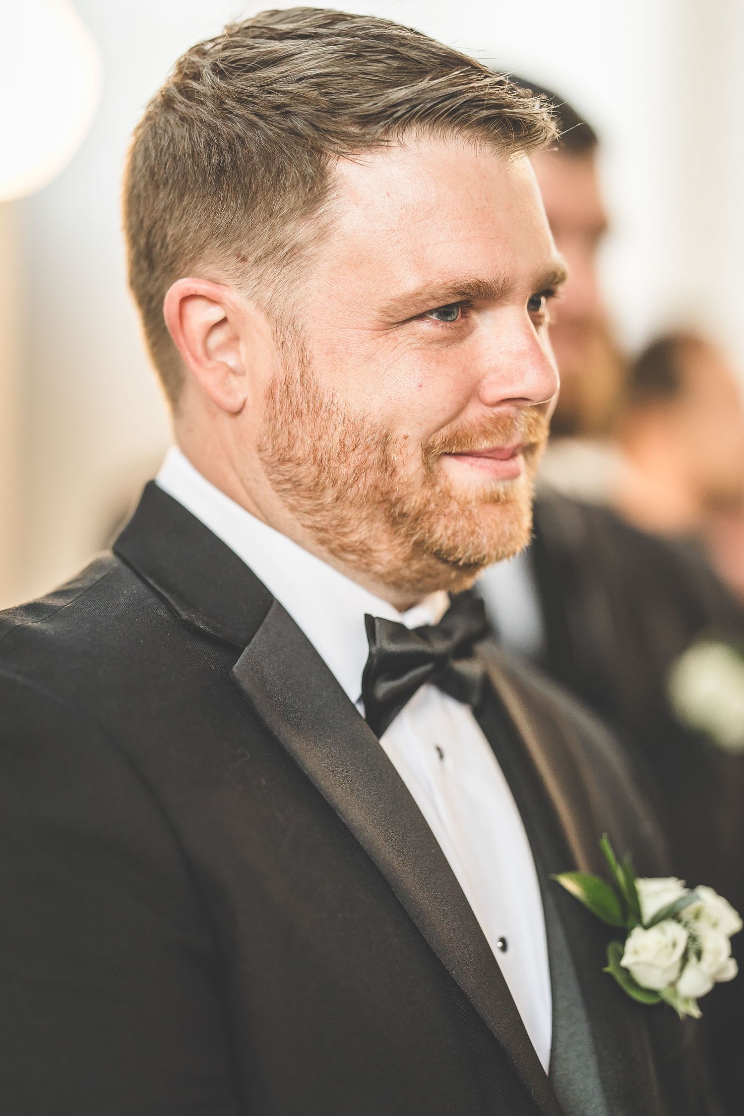 Close-up profile shot of groomsman wearing black tuxedo with white boutonniere.