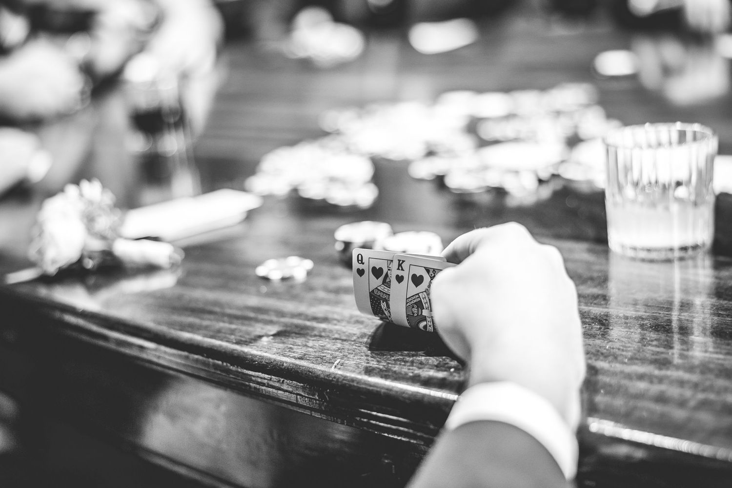 Playing cards and drinks scattered on a dark wooden table surface.