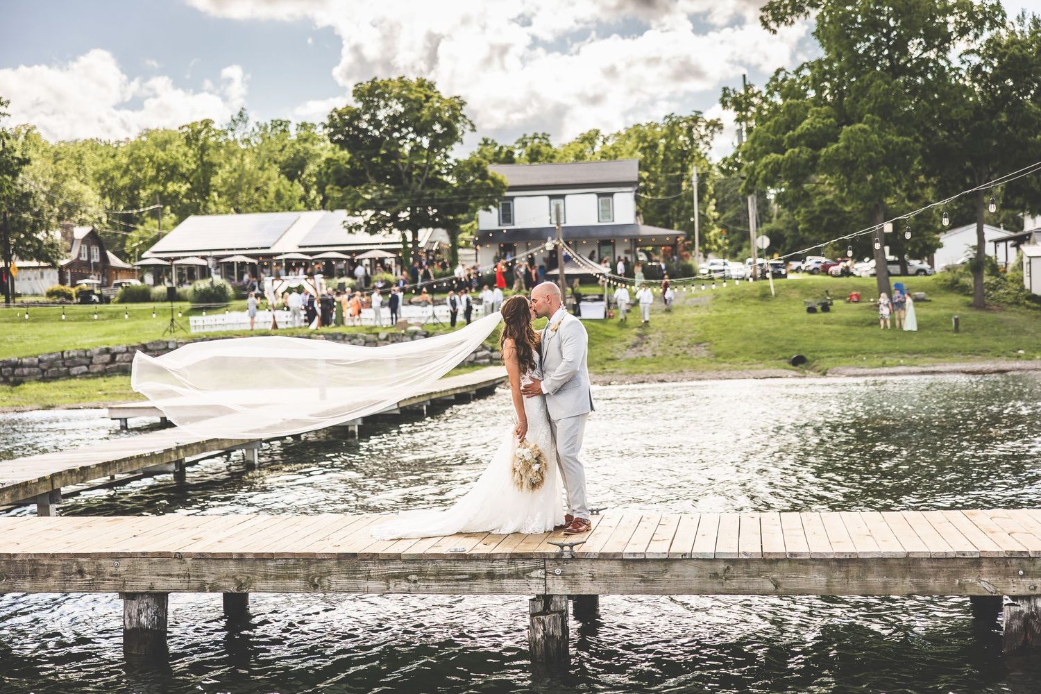Wedding party poses for photos on a wooden dock overlooking a serene lake.