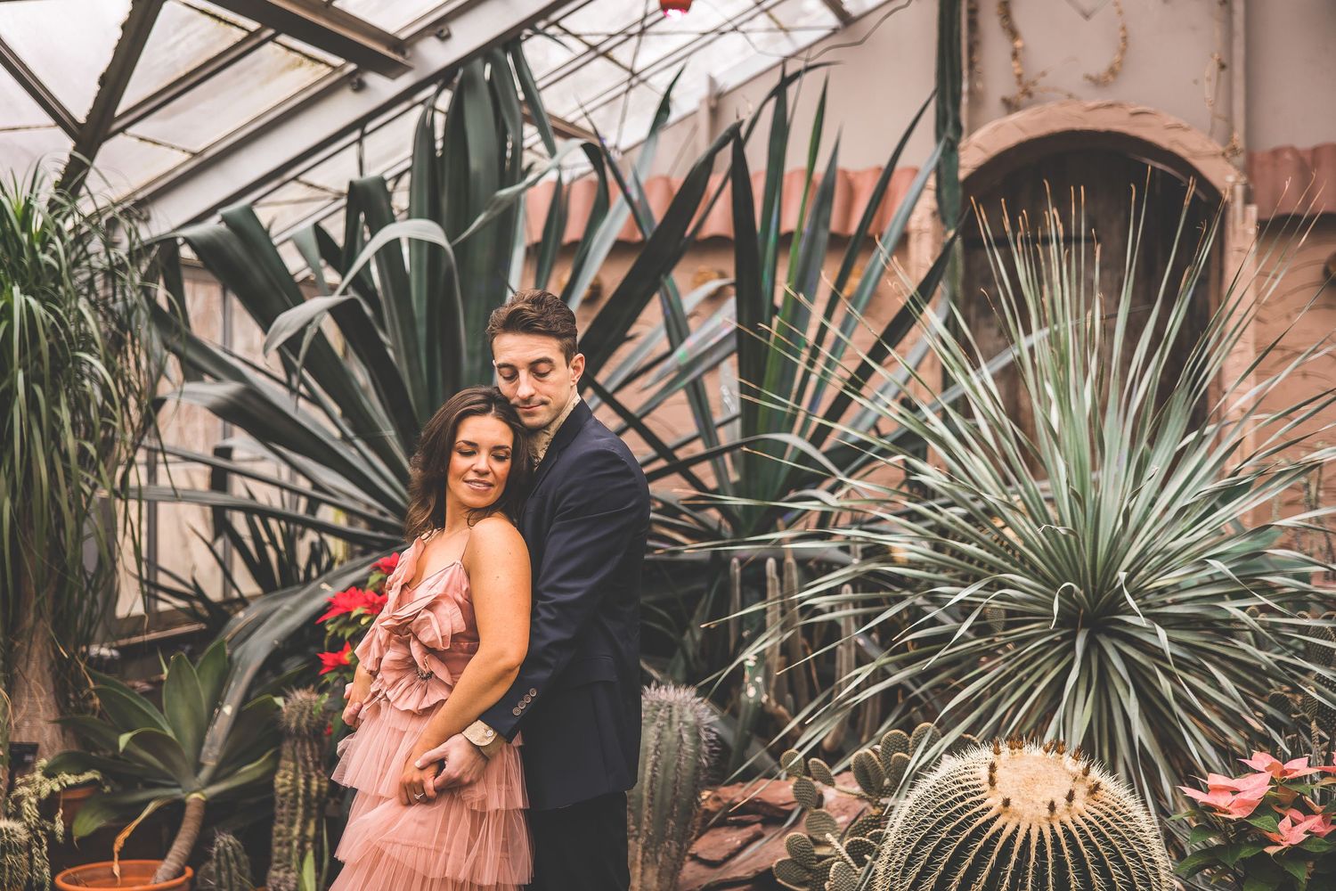 Greenhouse engagement session surrounded by tropical plants and palm fronds.