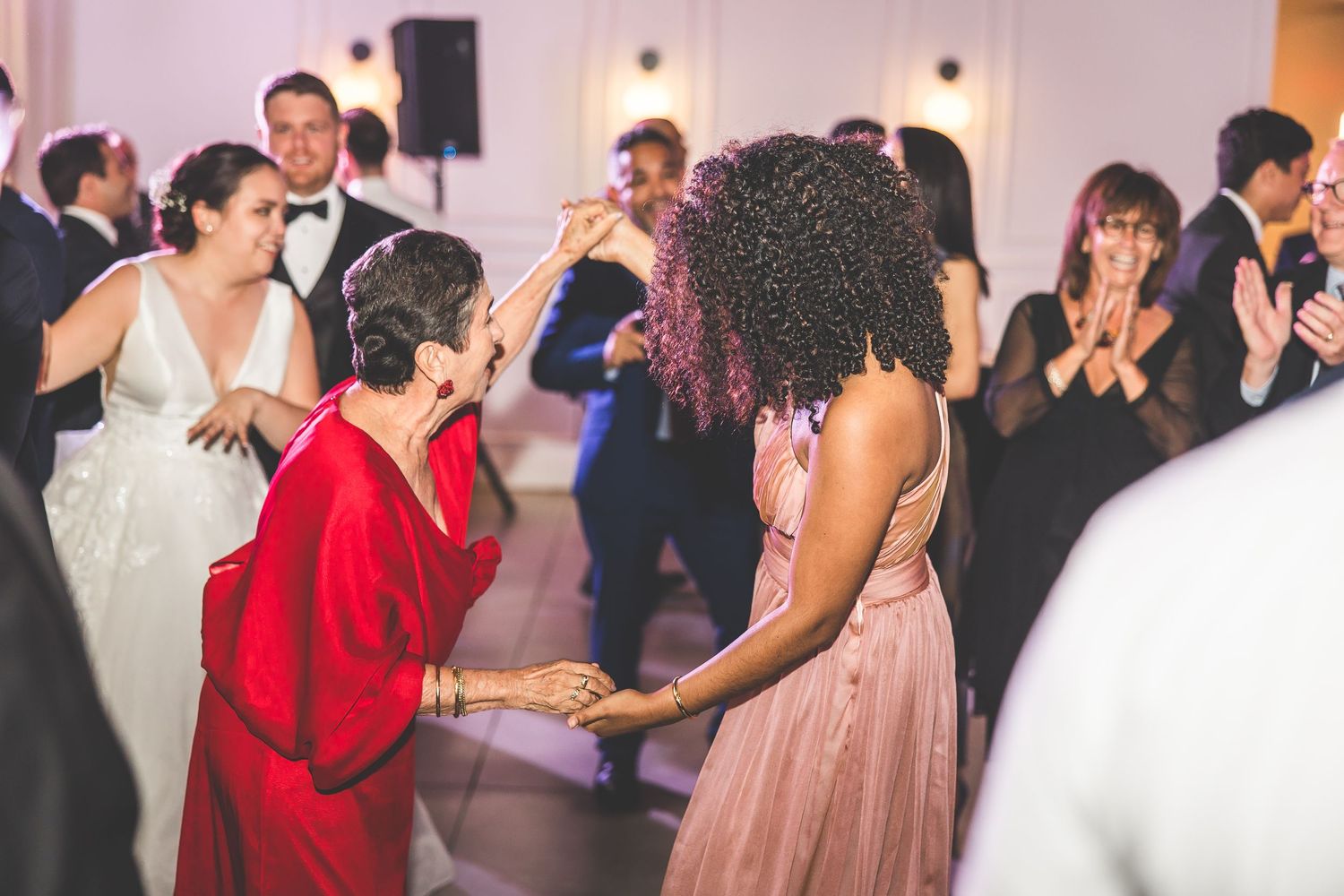 Wedding guests dancing and celebrating on a crowded dance floor with ambient lighting.