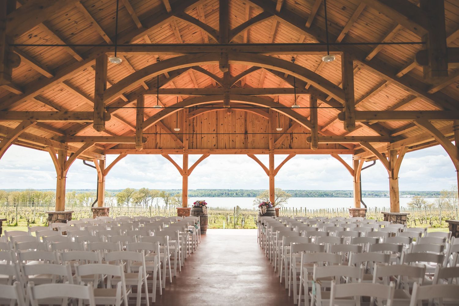 Rustic wooden pavilion set up for waterfront wedding ceremony with white chairs.