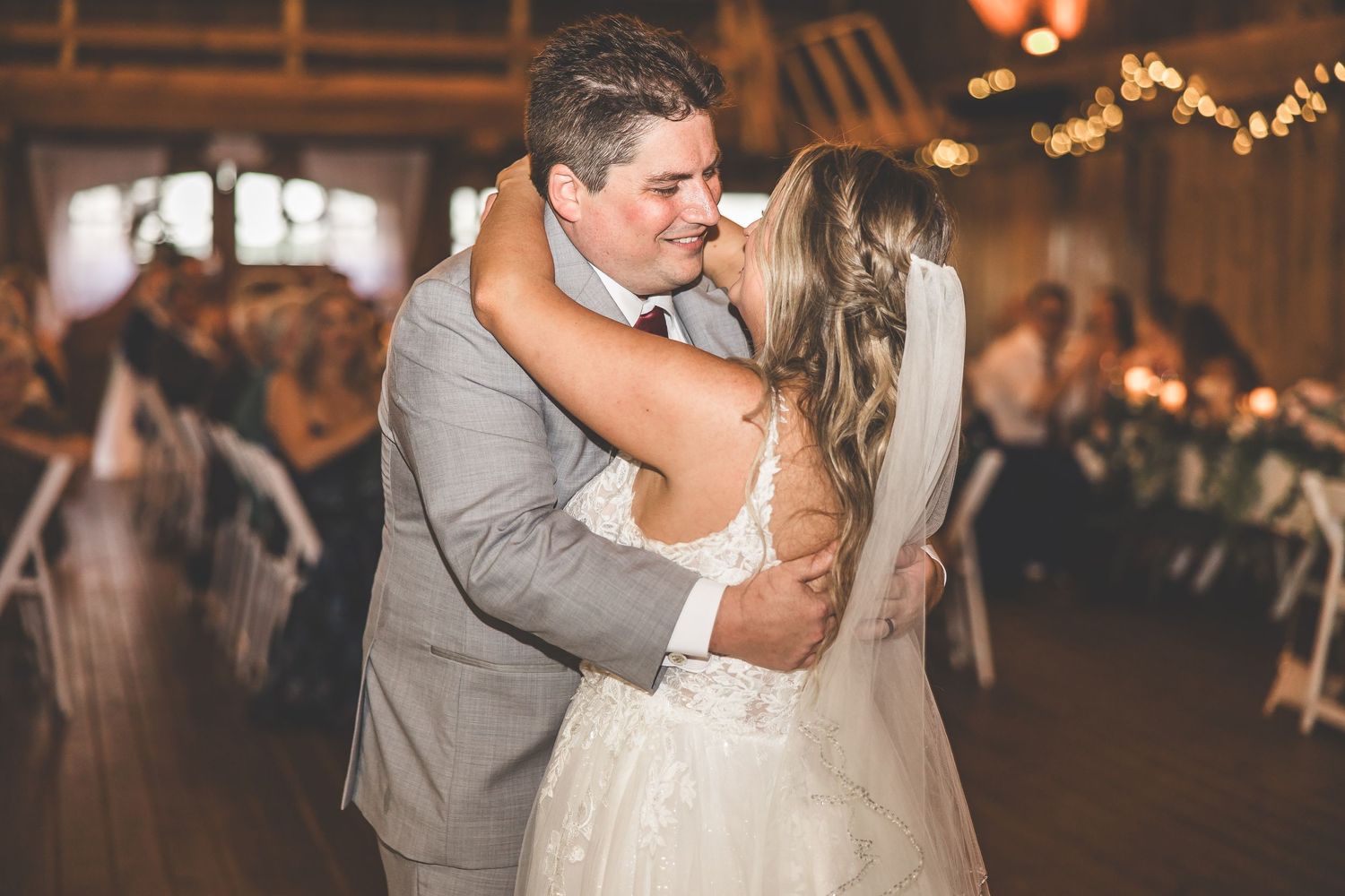 Romantic dance scene in rustic barn wedding reception with warm ambient lighting.