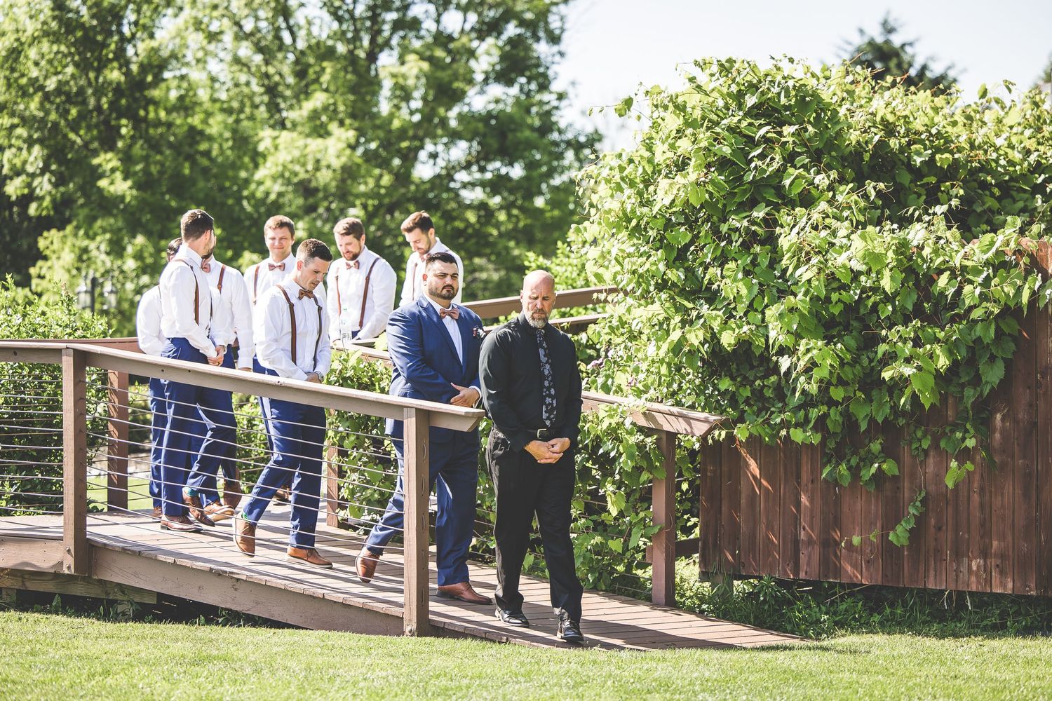 Wedding guests gather on a wooden deck surrounded by lush green trees and foliage.