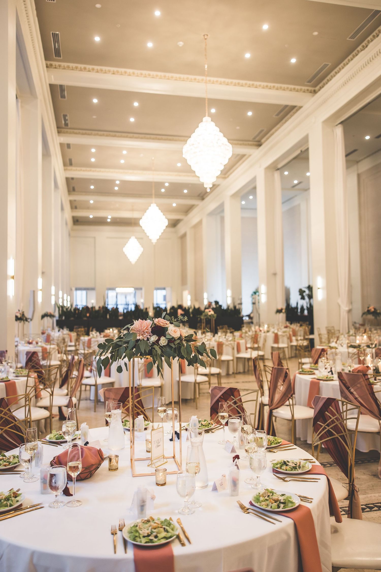 Spacious white ballroom set for wedding reception with crystal chandeliers and round tables.