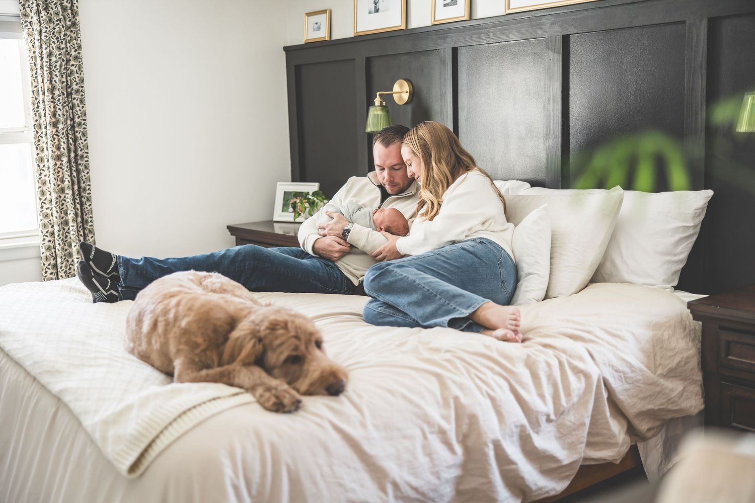 Family lounging on bed with newborn baby in cozy bedroom setting.