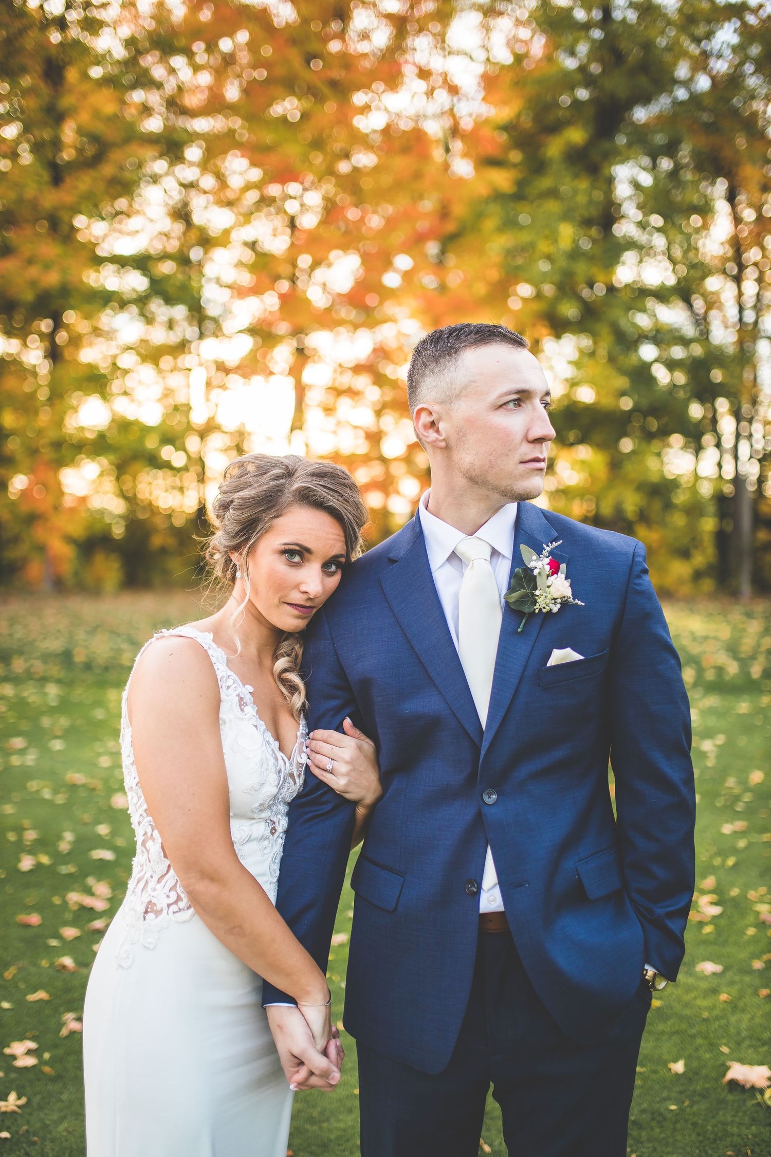 Couple poses for romantic autumn wedding photos in a field with golden sunlight filtering through trees.