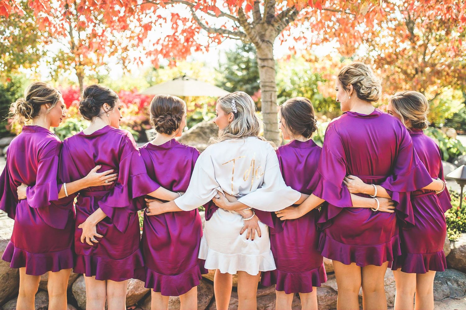 Wedding party in burgundy attire poses together during autumn with colorful fall foliage.