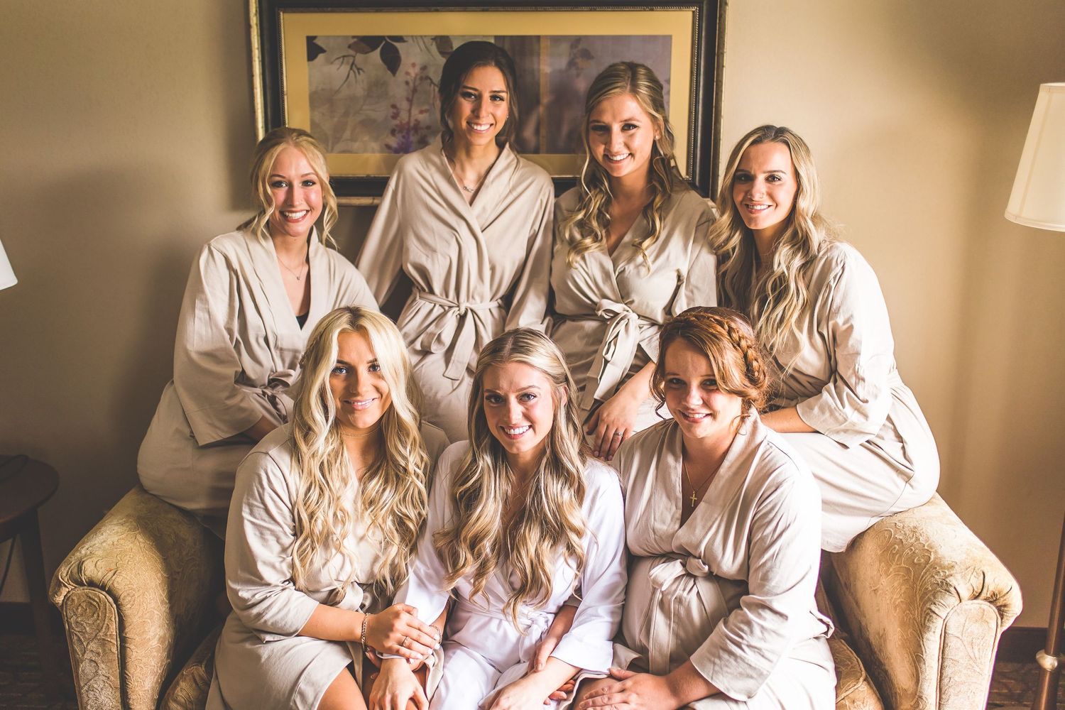 Bridal party in white robes sharing joyful moments during wedding preparations.