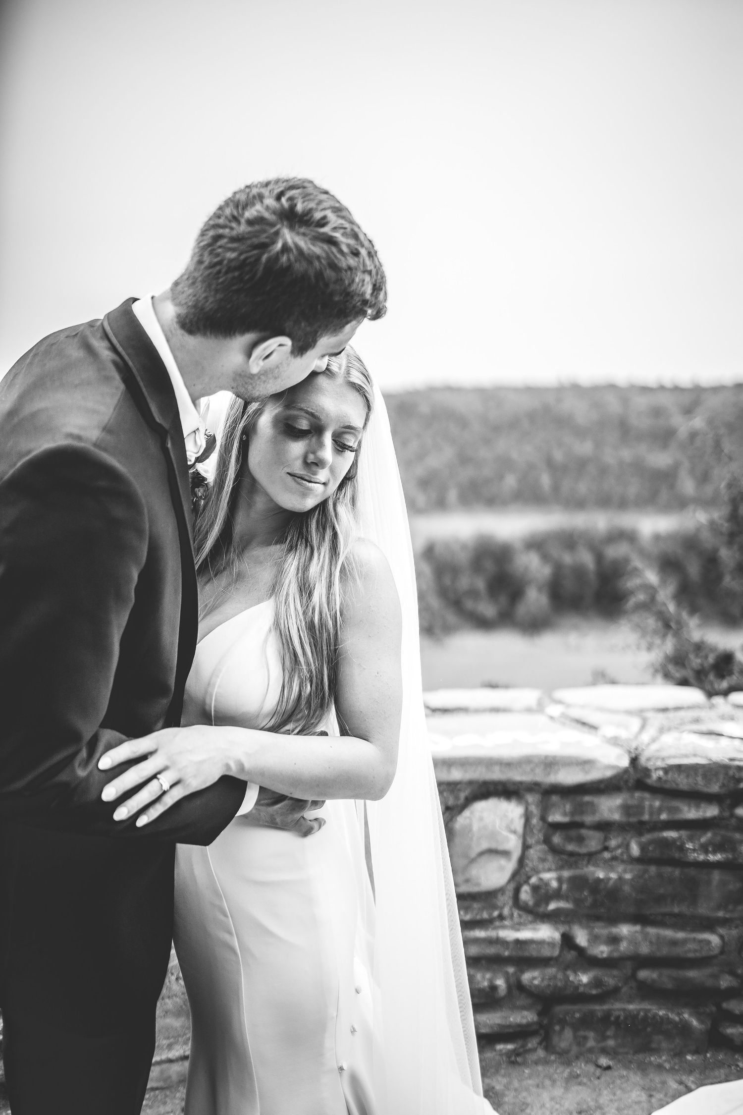 Black and white intimate wedding portraits captured against rustic stone wall backdrop.