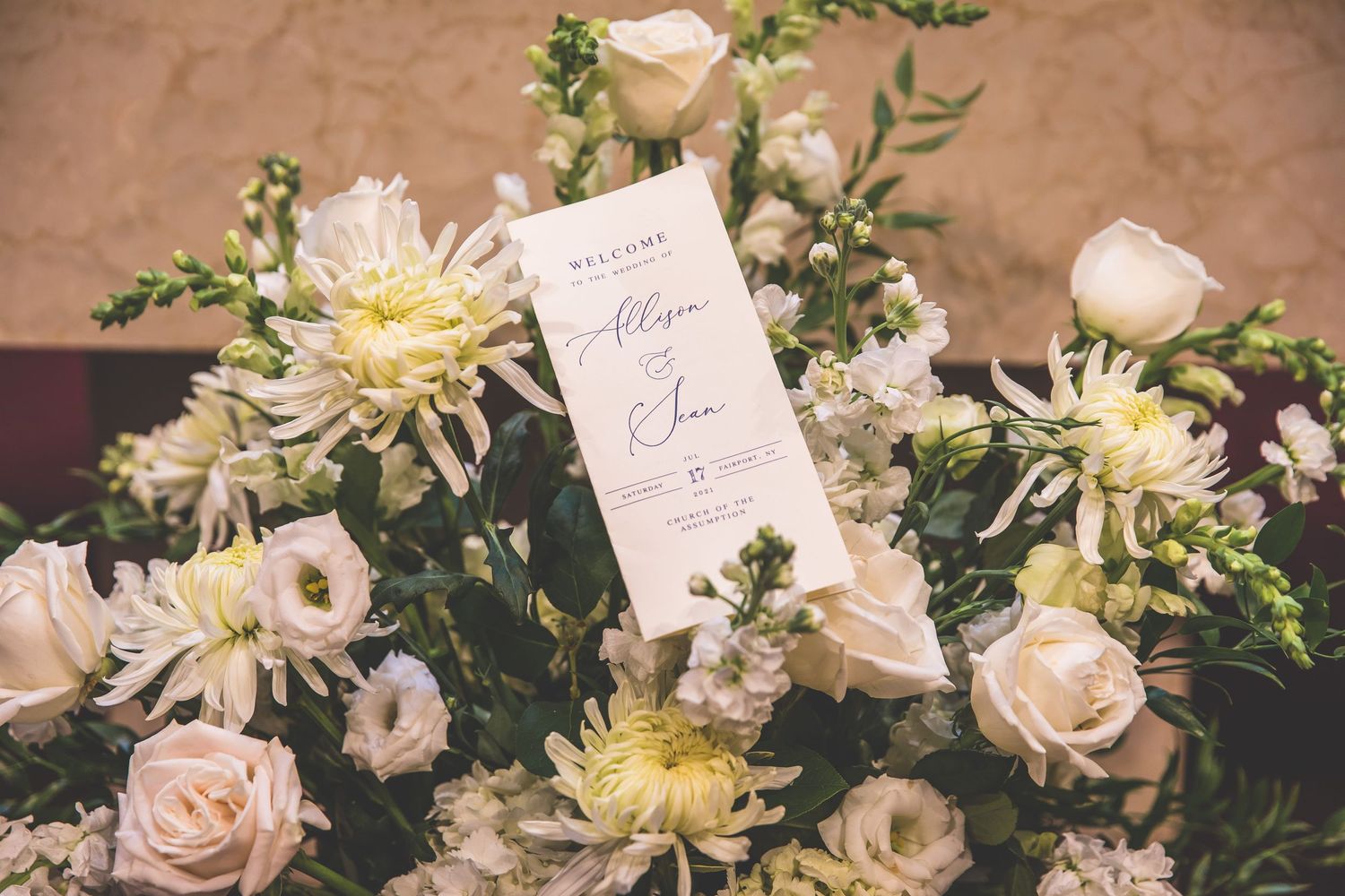 Elegant white and cream floral arrangements with roses and dahlias displayed with wedding stationery.