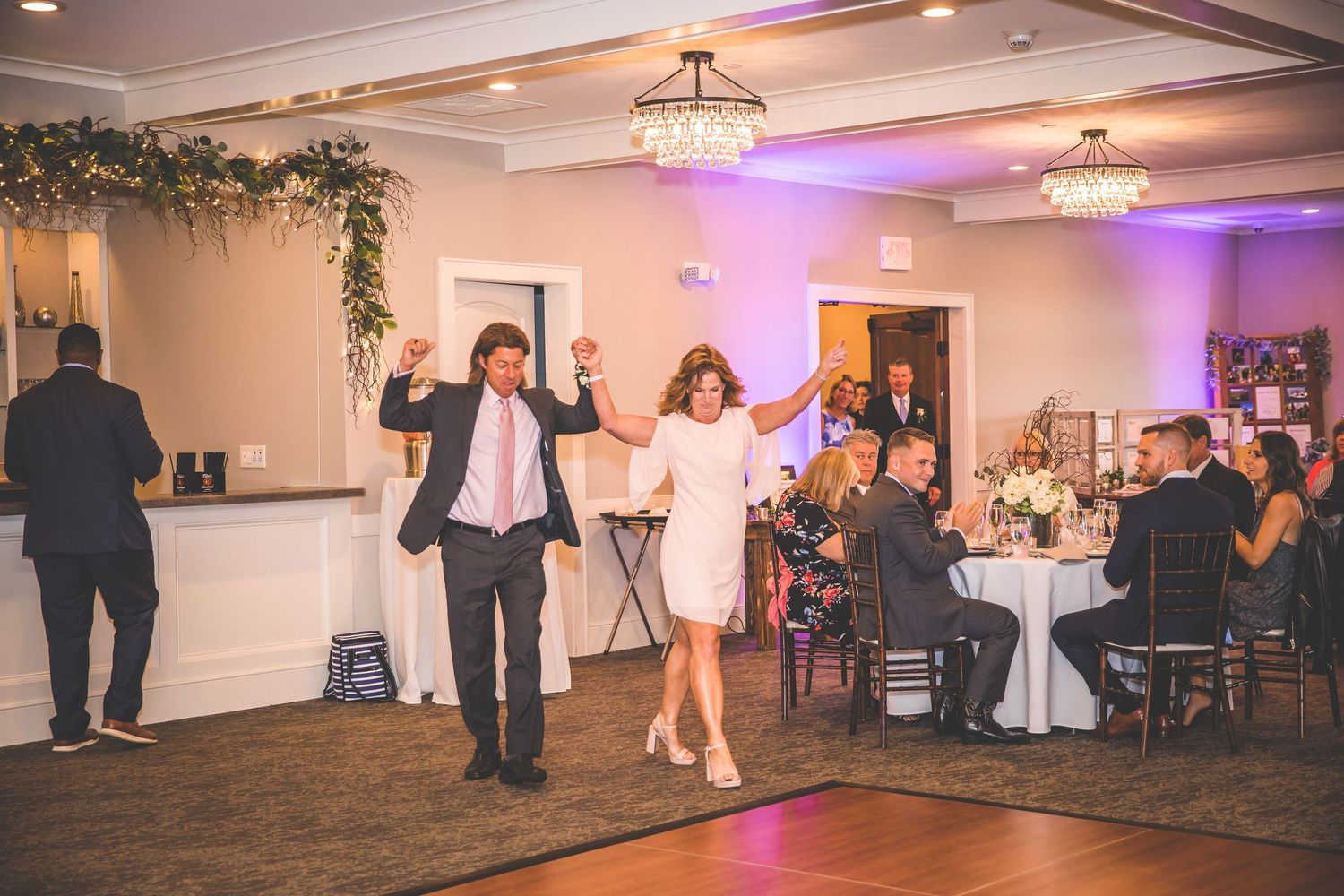 Wedding guests dancing and celebrating in an elegant ballroom with purple uplighting.
