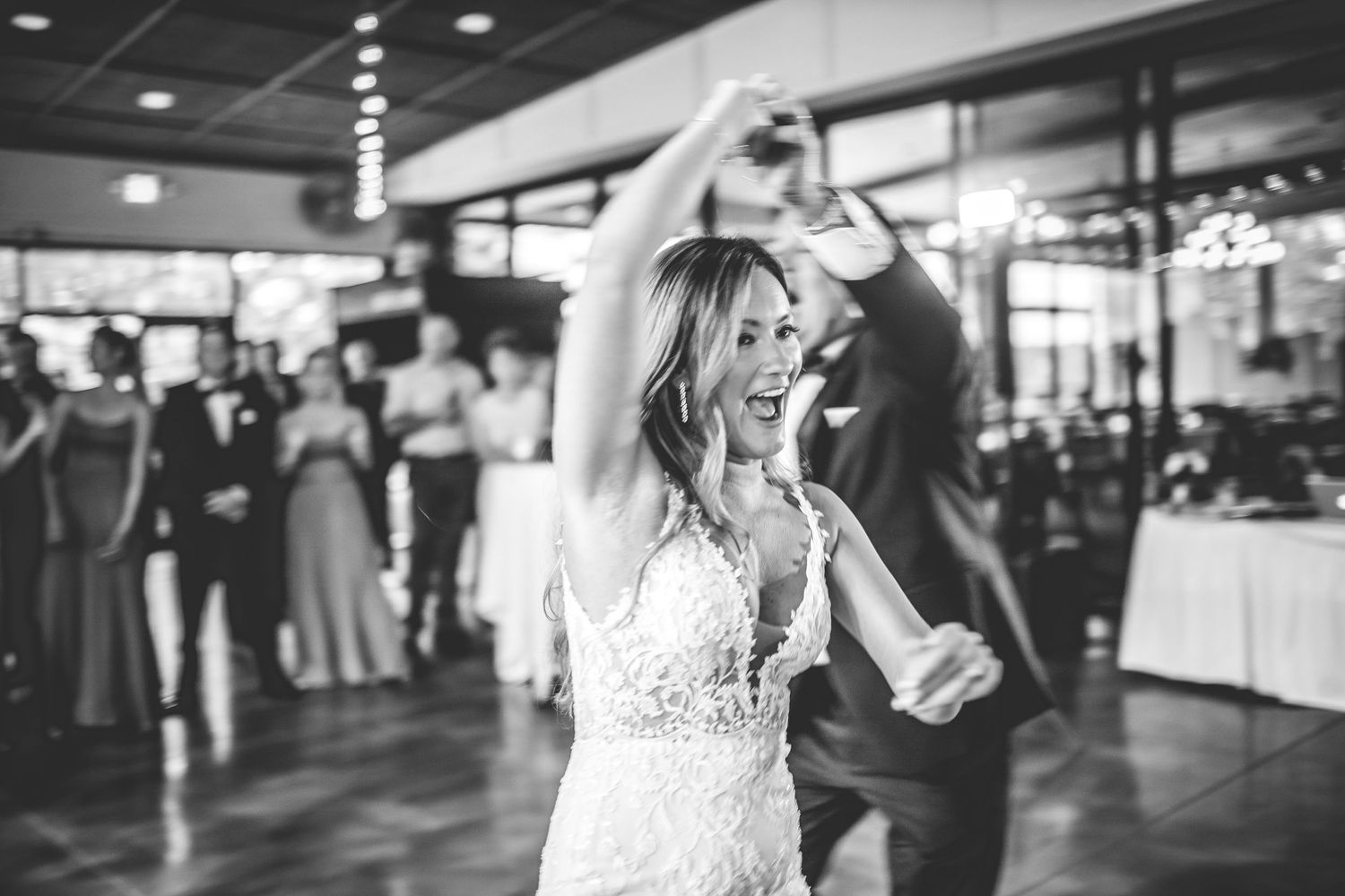 Black and white photo of joyful dancing during a wedding reception with string lights overhead.