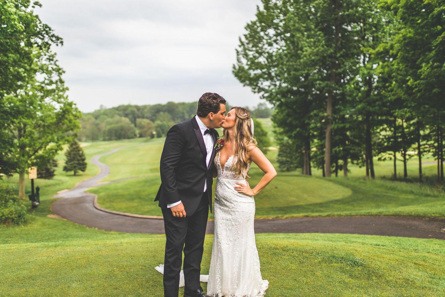 Newlyweds embrace on rolling green golf course landscape during wedding photoshoot.