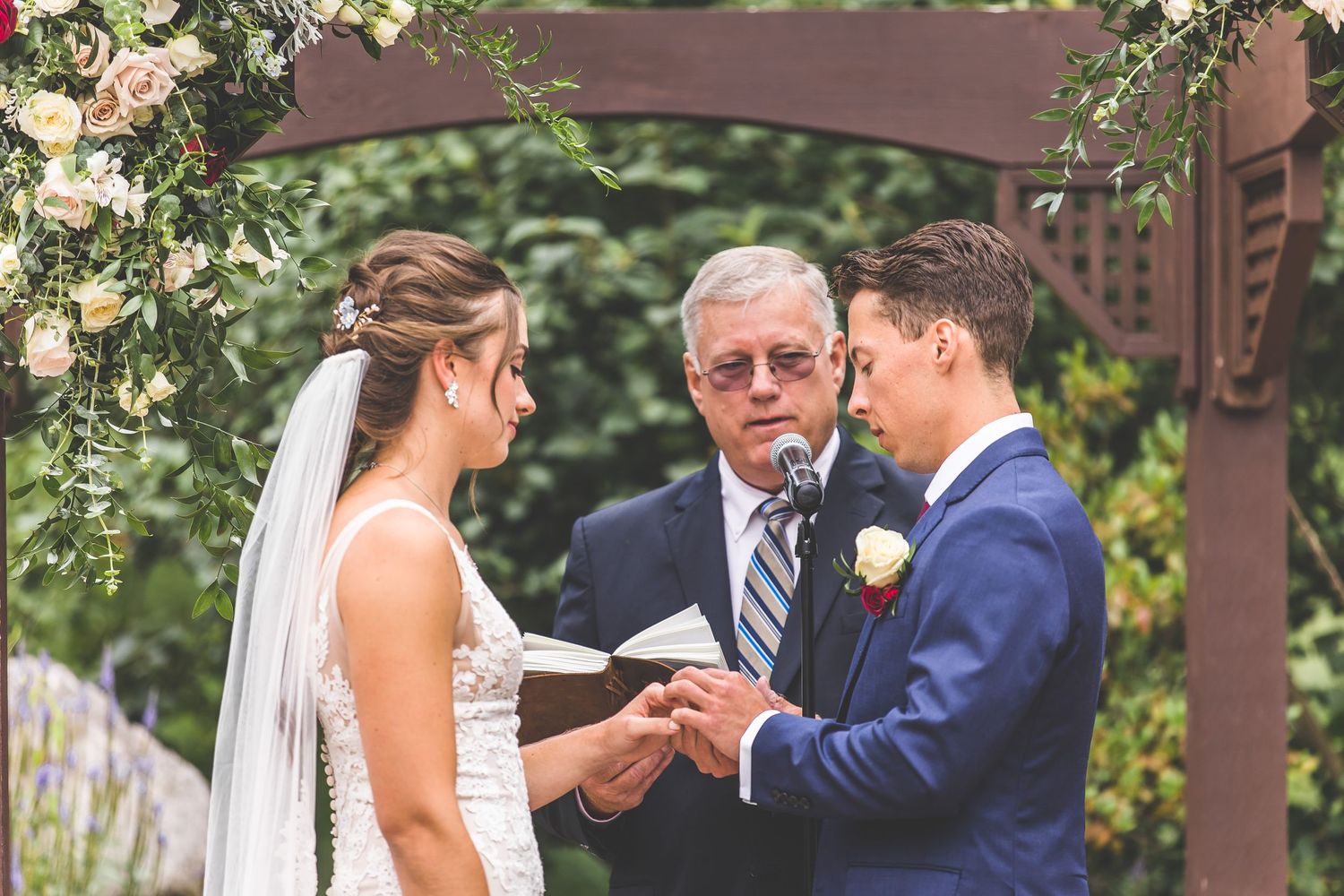 Intimate wedding ceremony moment under decorated wooden pergola with greenery backdrop.