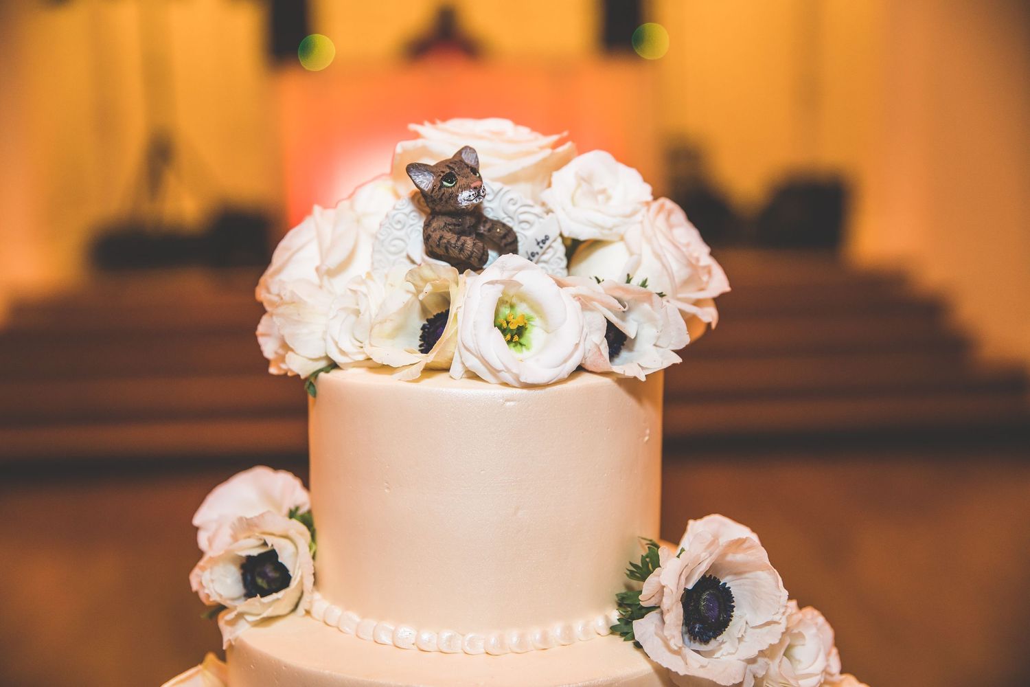 Close-up of a wedding cake decorated with delicate white and blush flowers against a warm amber background.