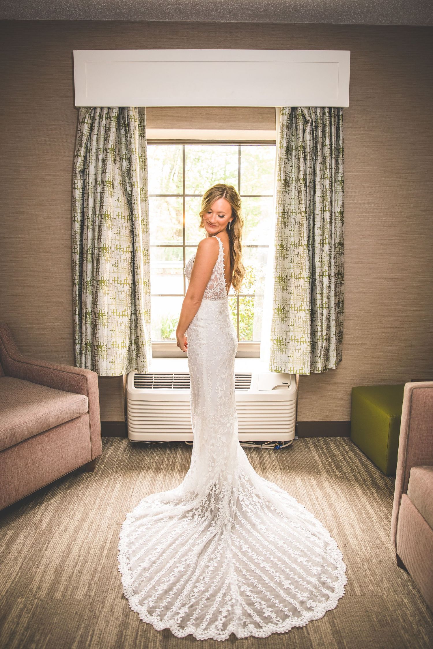 A stunning white lace wedding dress with a dramatic long train photographed against a window in a hotel room.