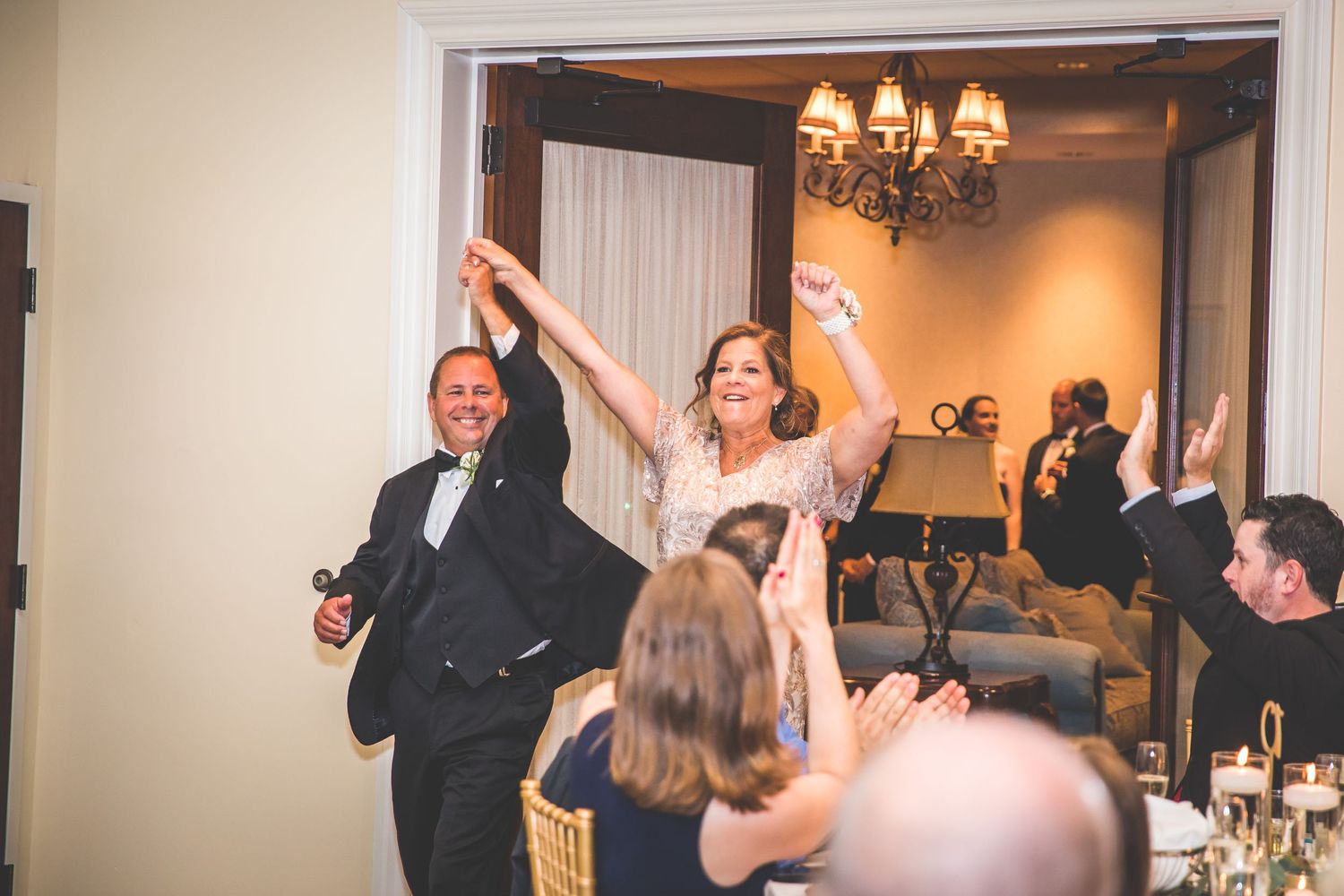 Wedding reception guests celebrate with raised arms in elegant indoor venue.