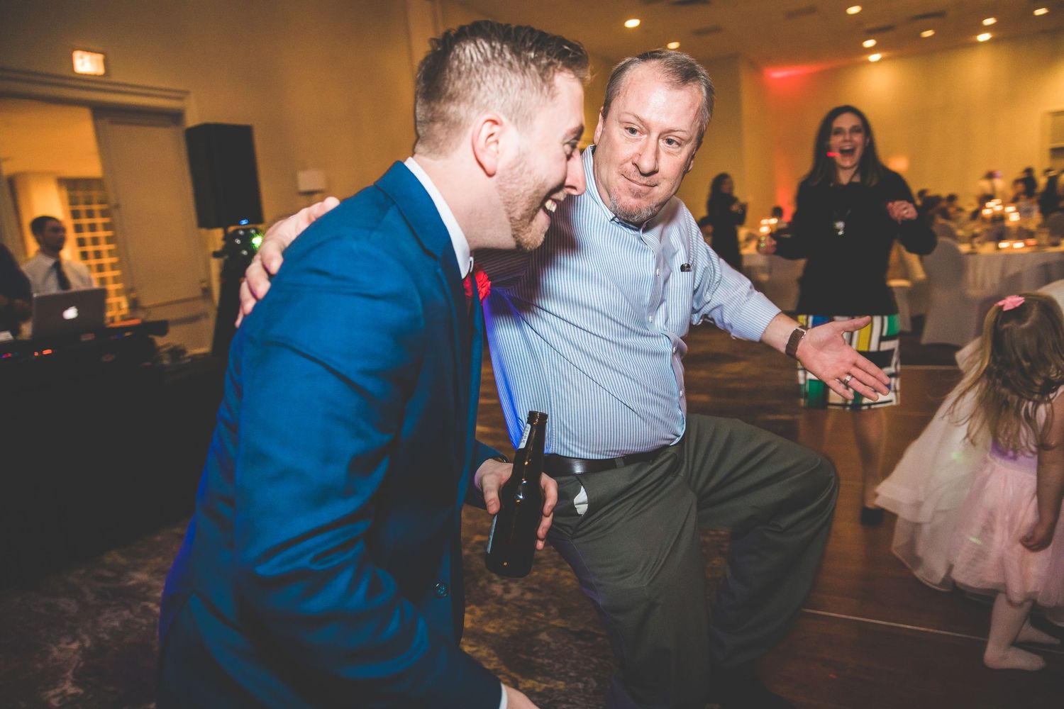 Guests dancing and socializing at an indoor wedding reception with colorful lighting.