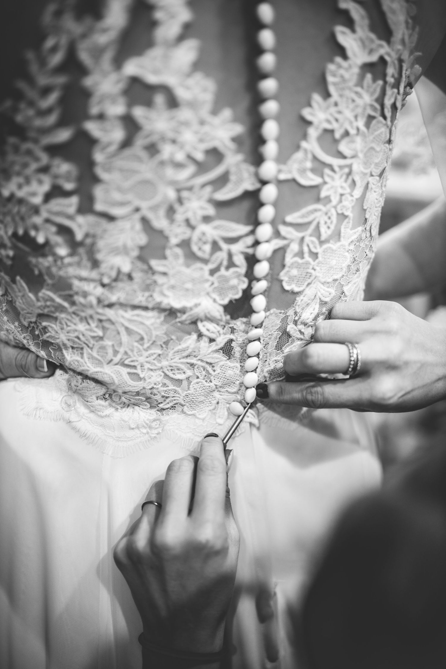 Close-up details of intricate lace and buttons being fastened on a wedding dress.