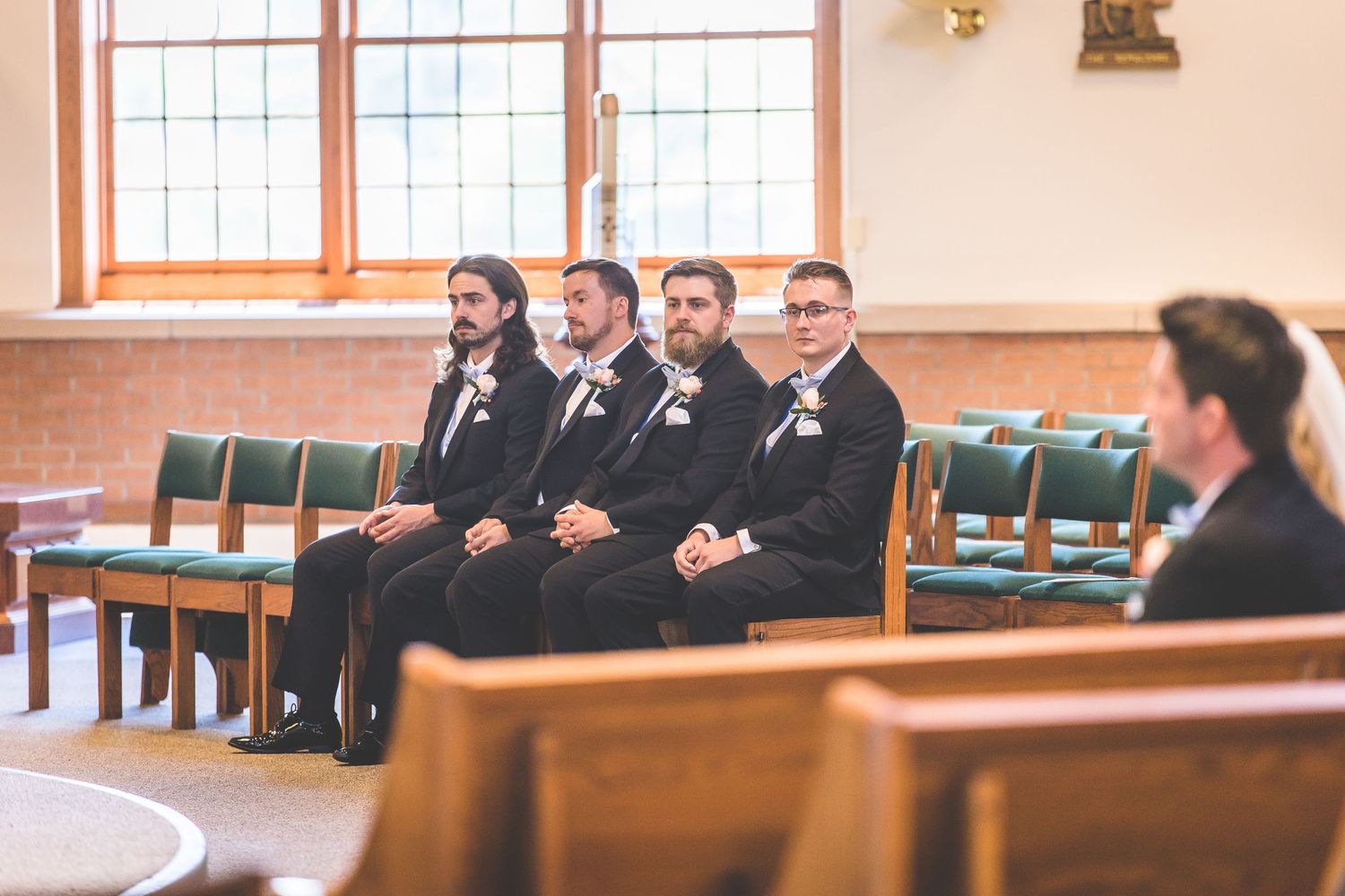 Wedding party lined up in church with wooden pews and large windows.
