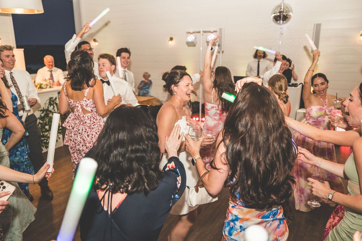 Wedding guests dance and wave glowing foam sticks during an indoor reception party.
