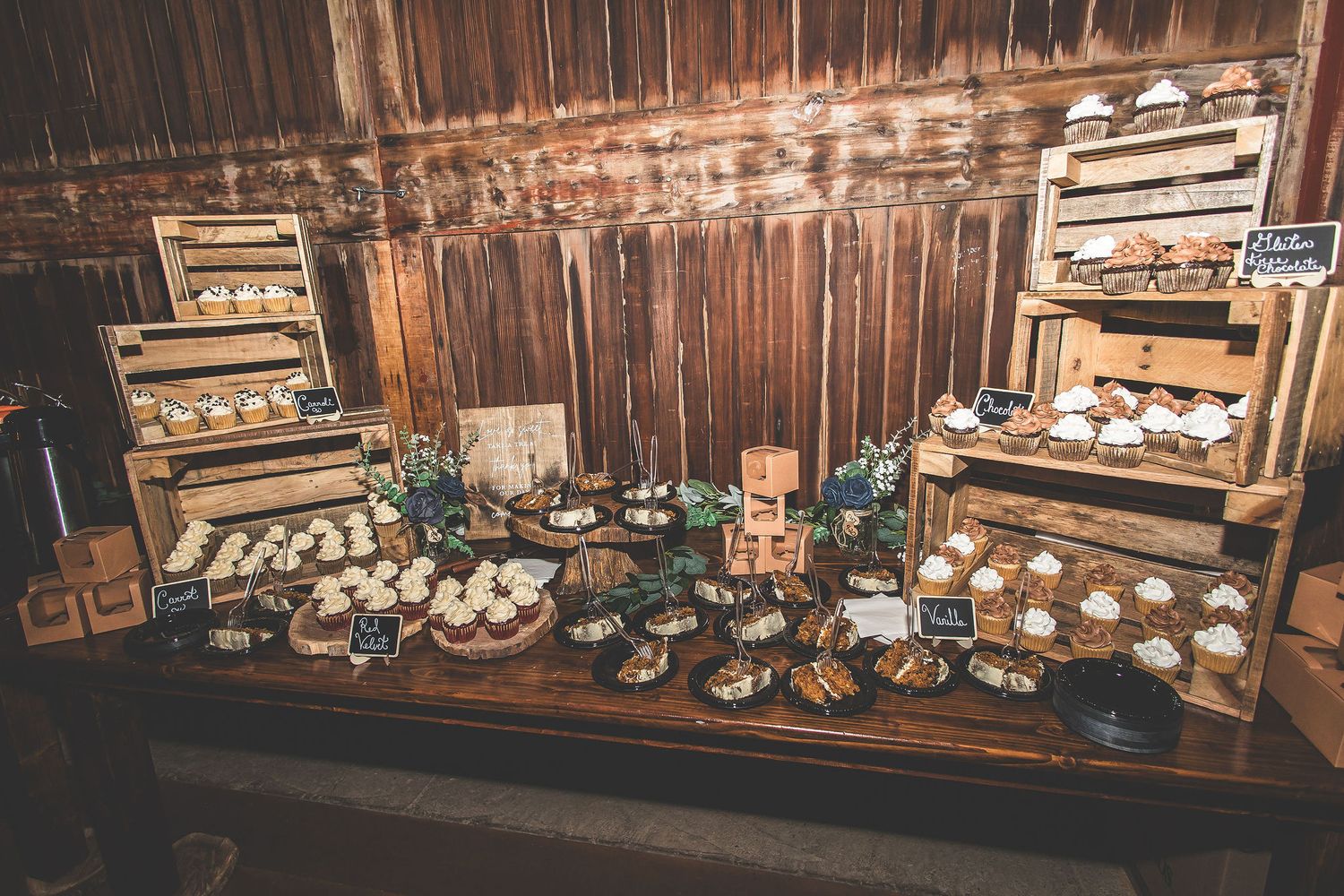 Rustic dessert table display with multiple tiers of treats against wooden barn wall.