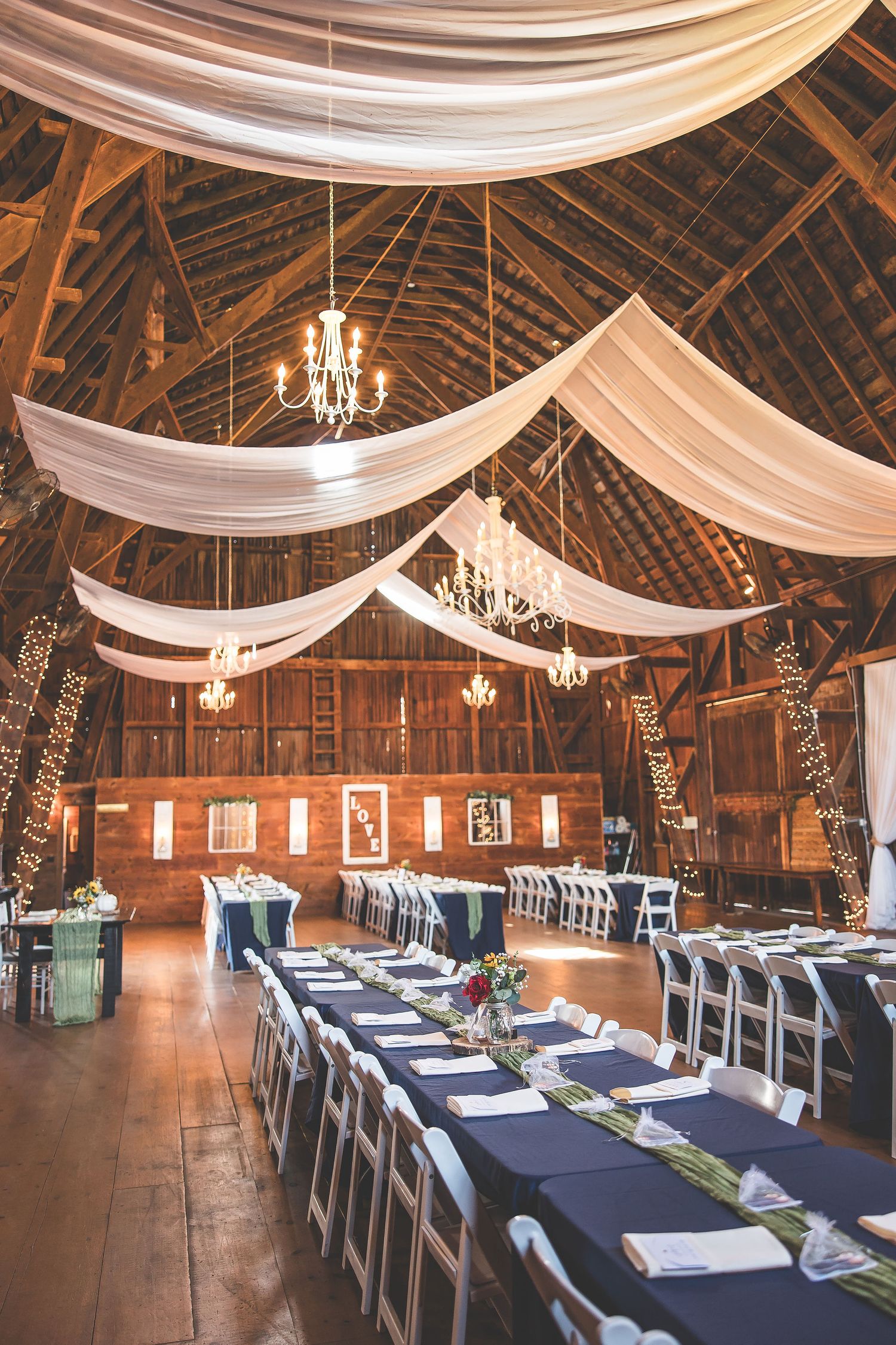 Rustic barn wedding venue with white fabric draping and chandeliers decorating the ceiling.