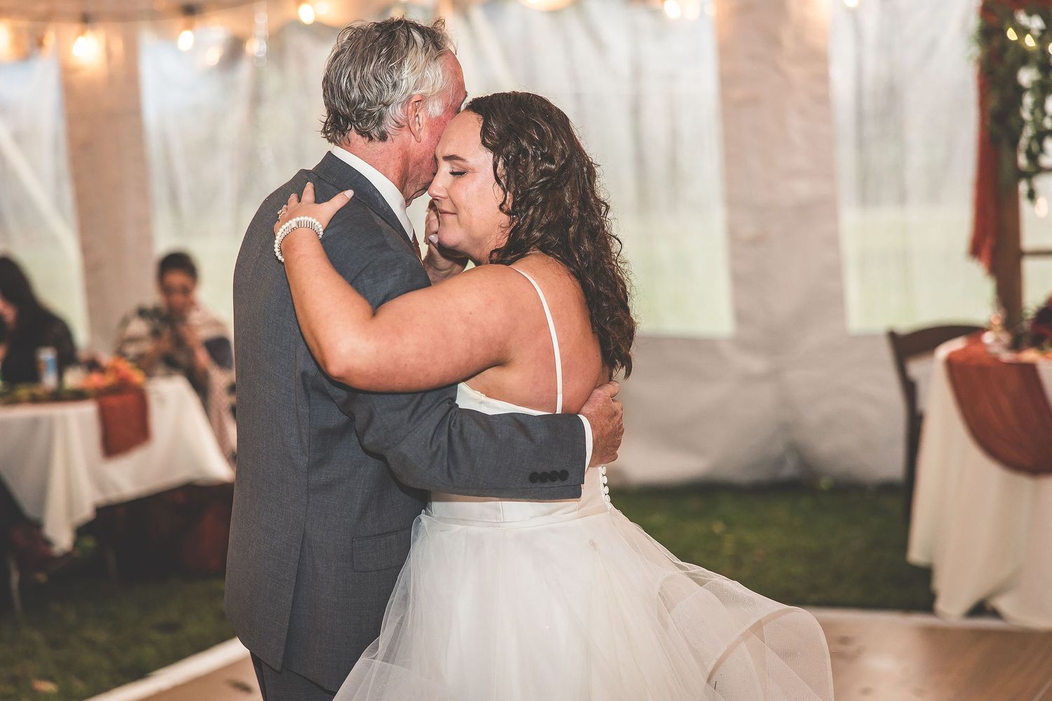 Wedding dance captured in romantic lighting with guests watching in elegant tent venue.