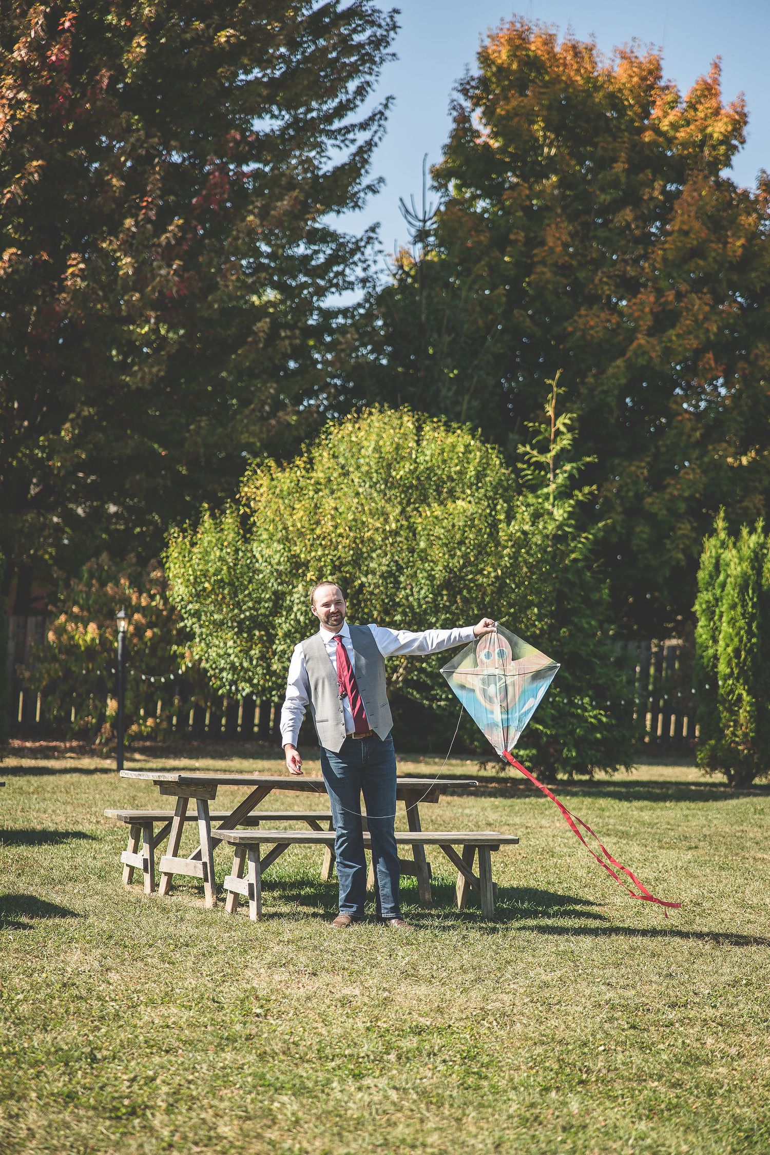 Couple flies kites in grassy field with autumn trees in background.