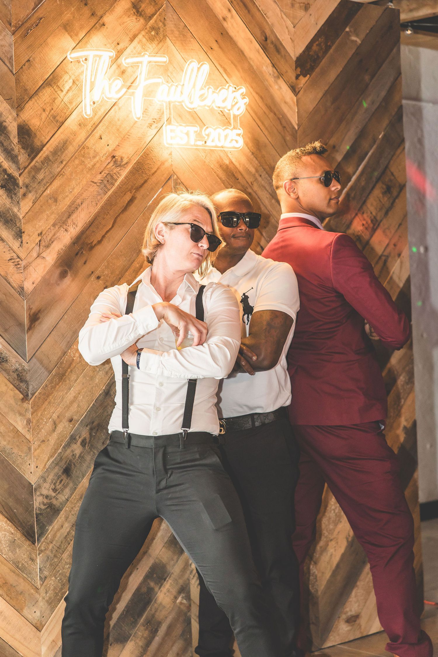Party guests pose playfully against a wooden wall with neon signage in the background.