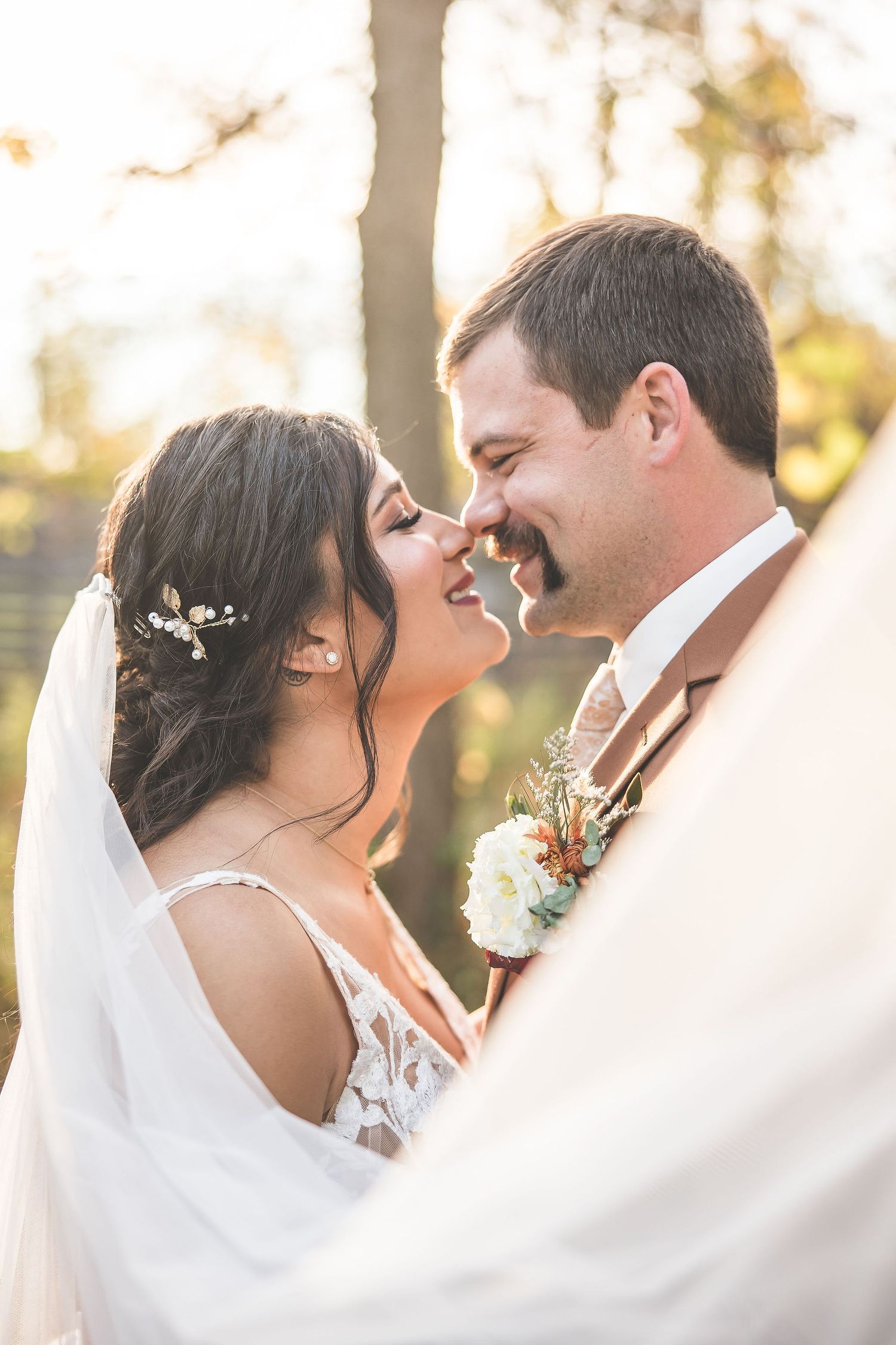 Intimate wedding moment captured through sheer white veil with golden sunlight in background.