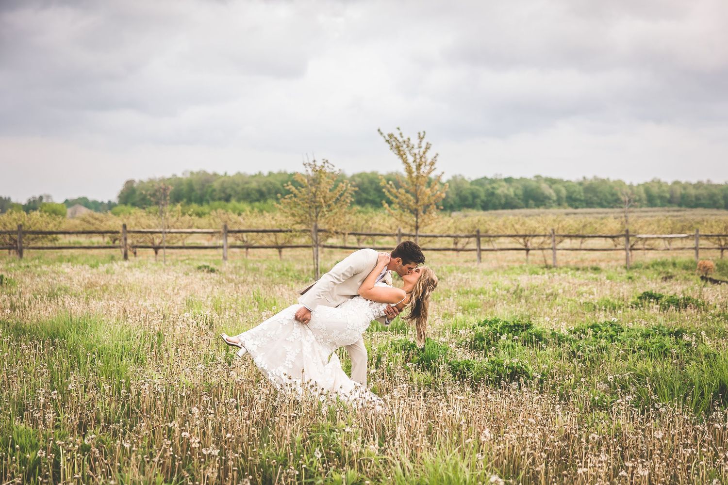 Wedding couple poses in a scenic meadow with rustic wooden fencing in the background.