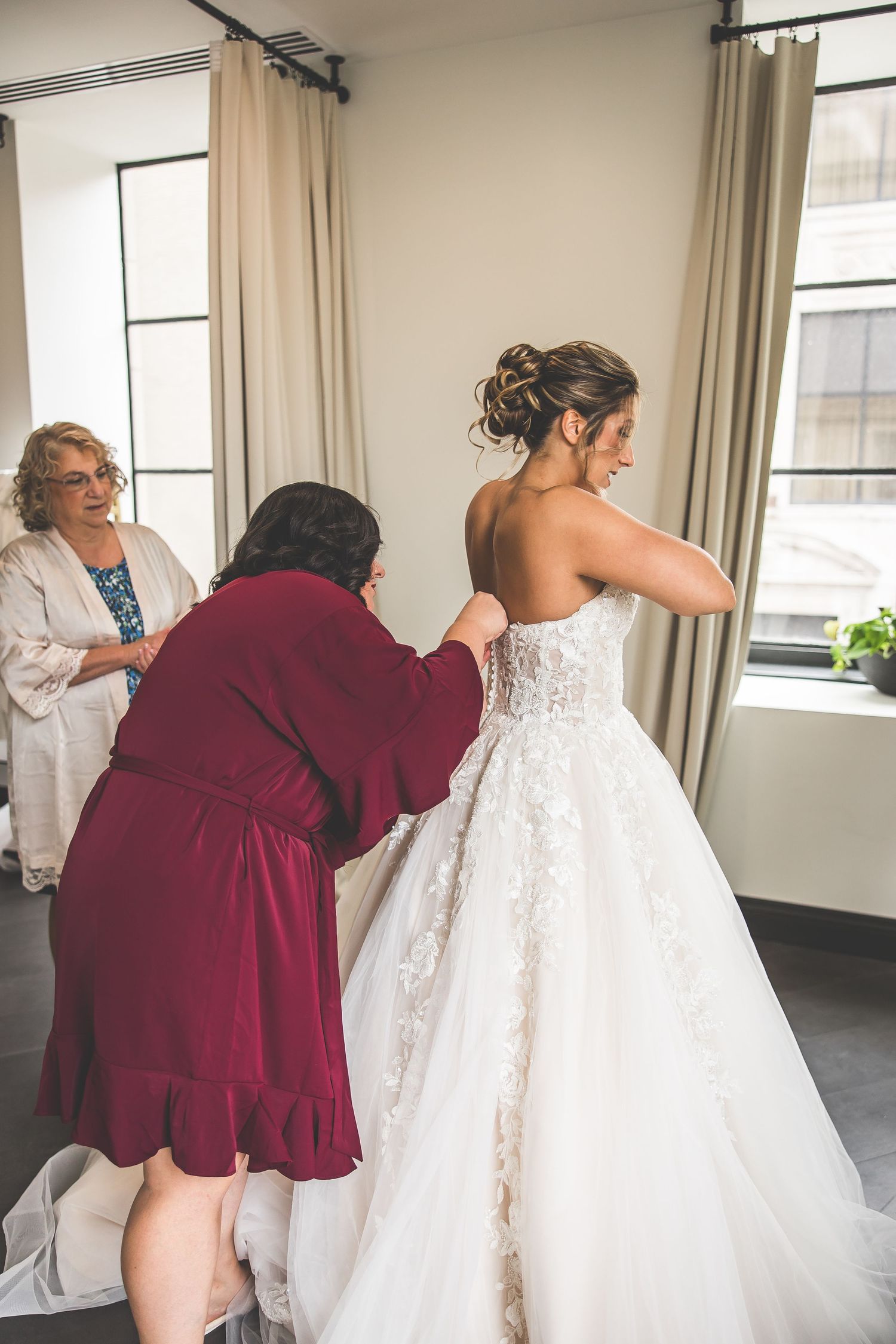 Wedding dress being adjusted and prepared with helpers in burgundy robes.