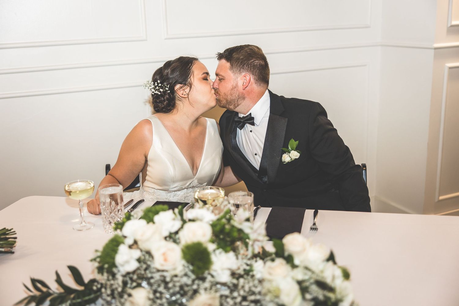 A couple shares an intimate moment at their sweetheart table decorated with white floral arrangements.