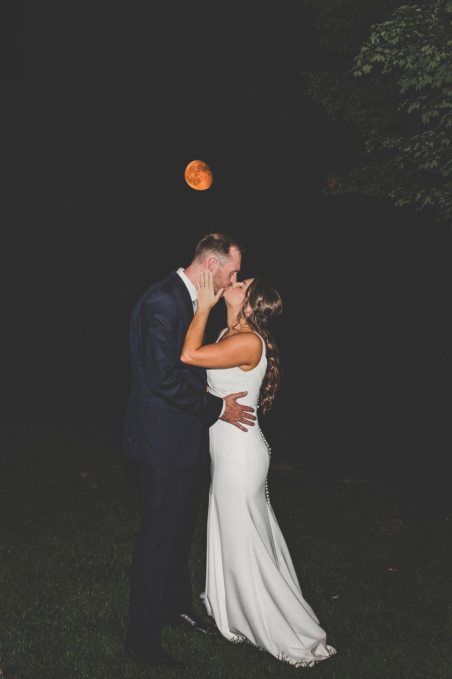 Romantic nighttime portrait with orange full moon glowing in dark sky.