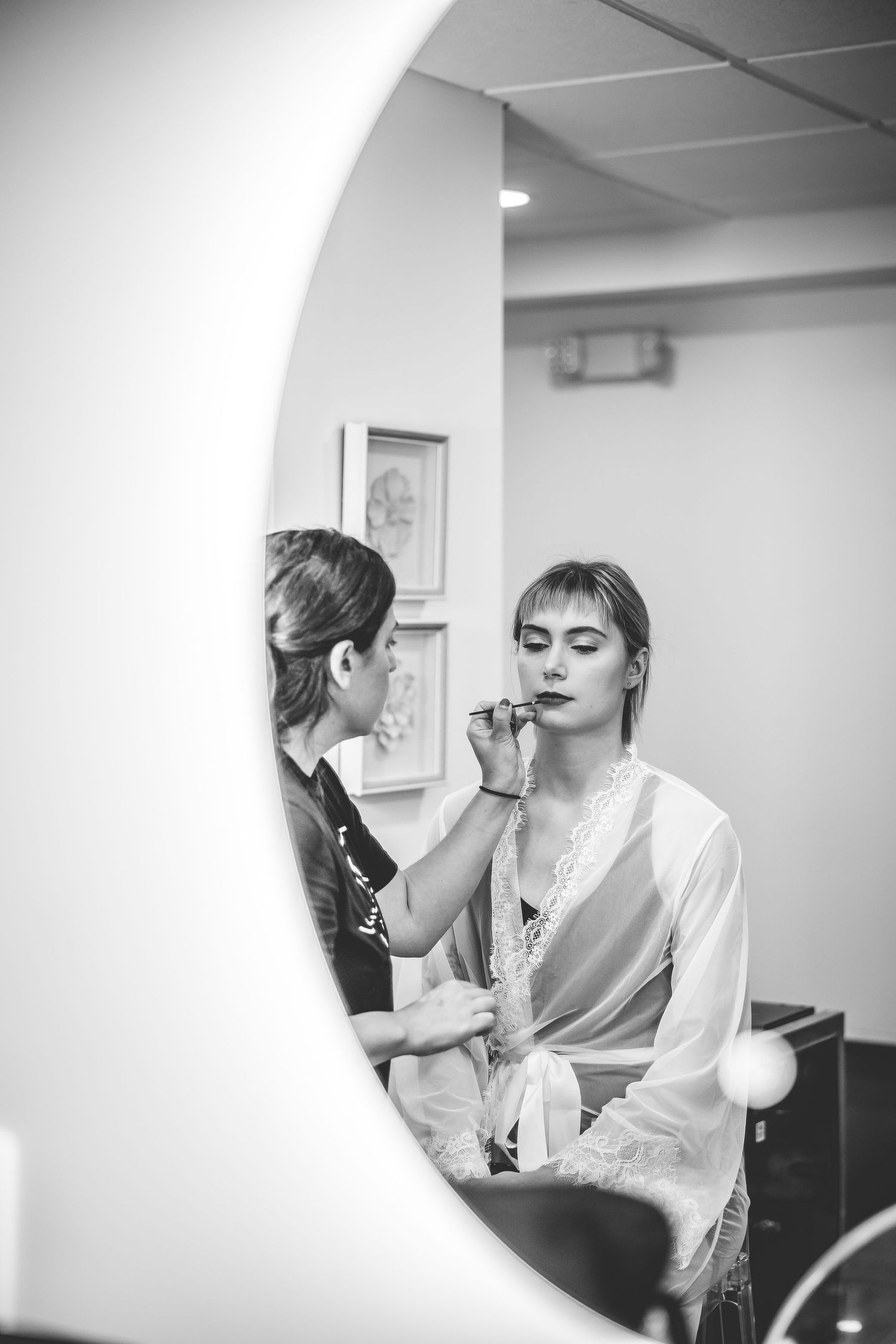 Black and white photo of wedding makeup preparation in a bright room.