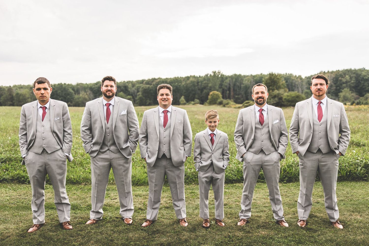 Wedding party in matching grey suits standing in formation on grassy field.