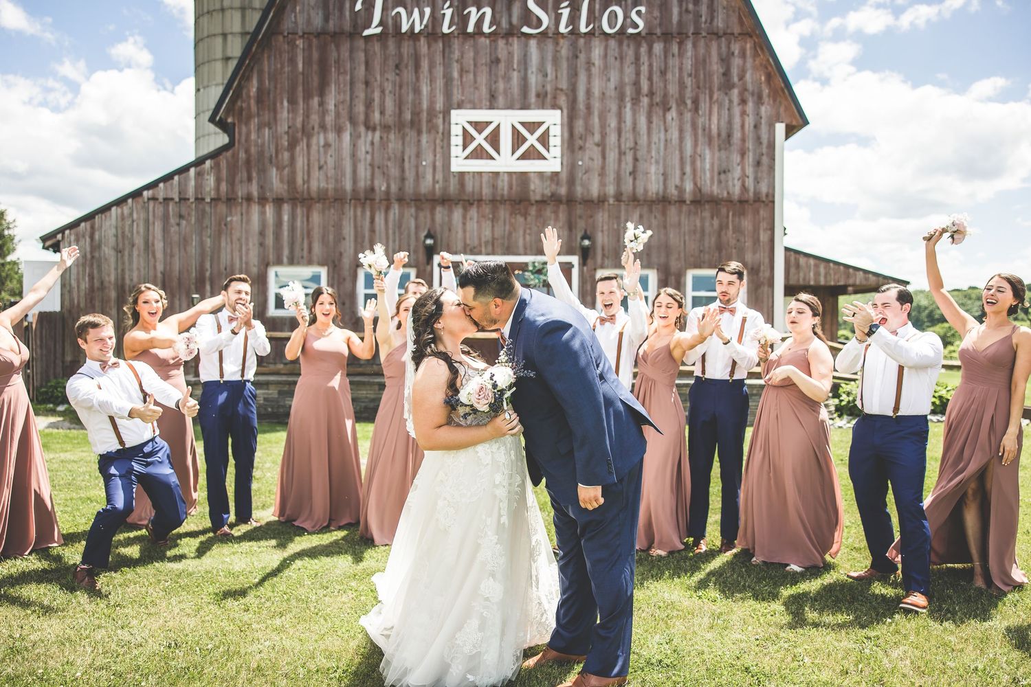 Rustic barn wedding venue with Twin Silos sign and wedding party posing in front.
