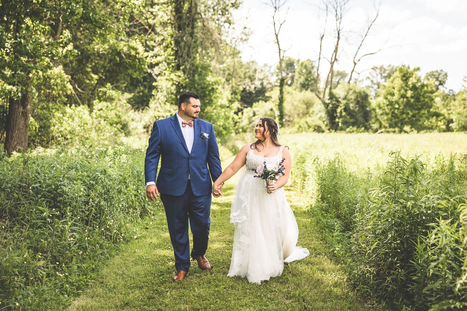 Wedding couple walking through a lush green field on their special day.