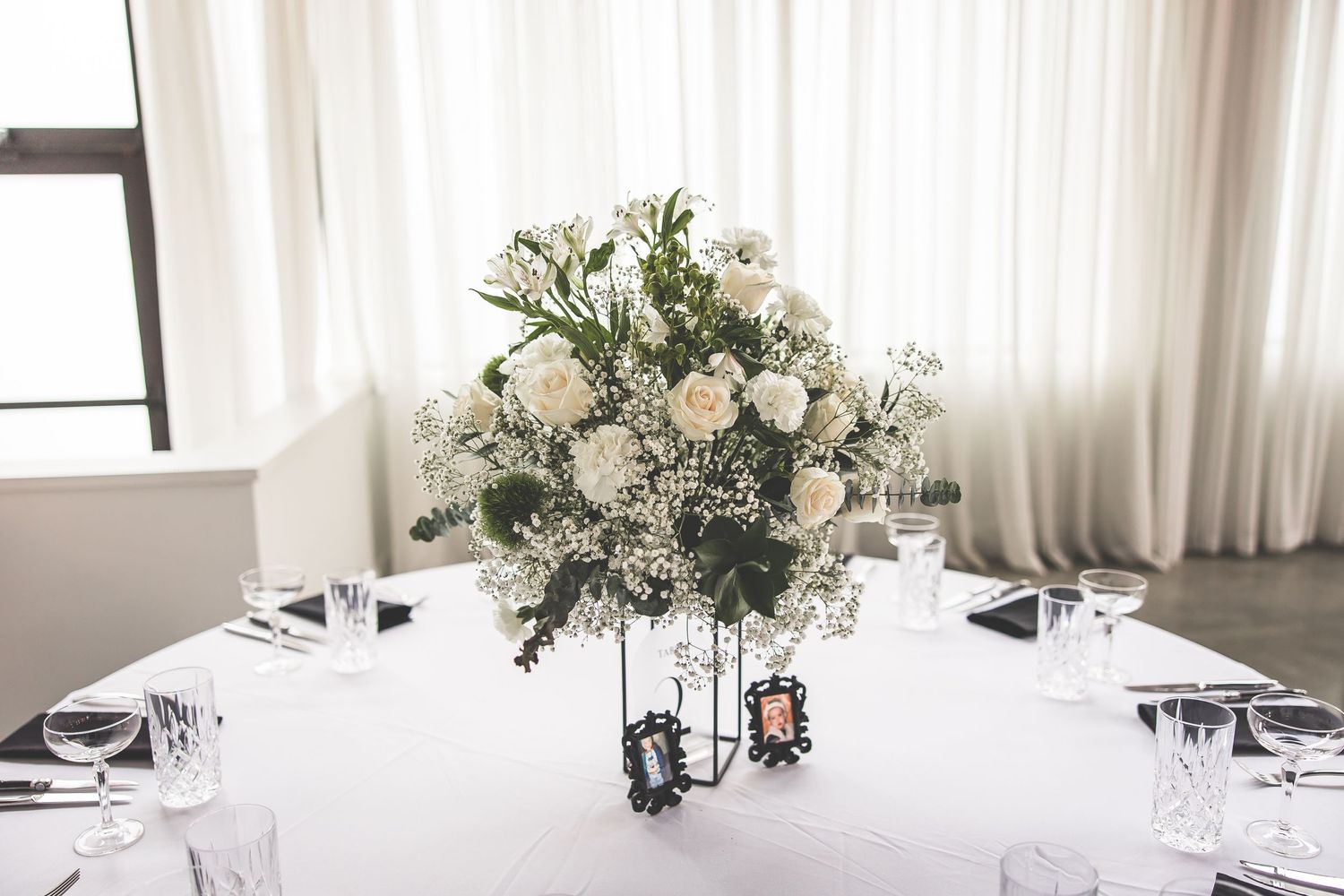 Elegant white floral centerpiece with roses and greenery on round reception table.