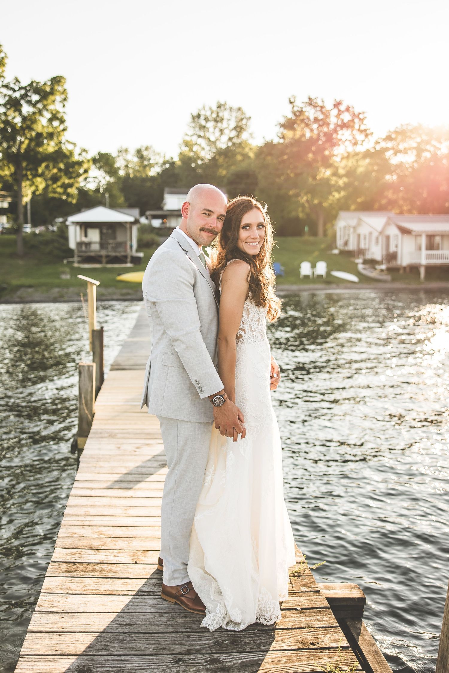 Couple poses on wooden dock at sunset with lake in background.