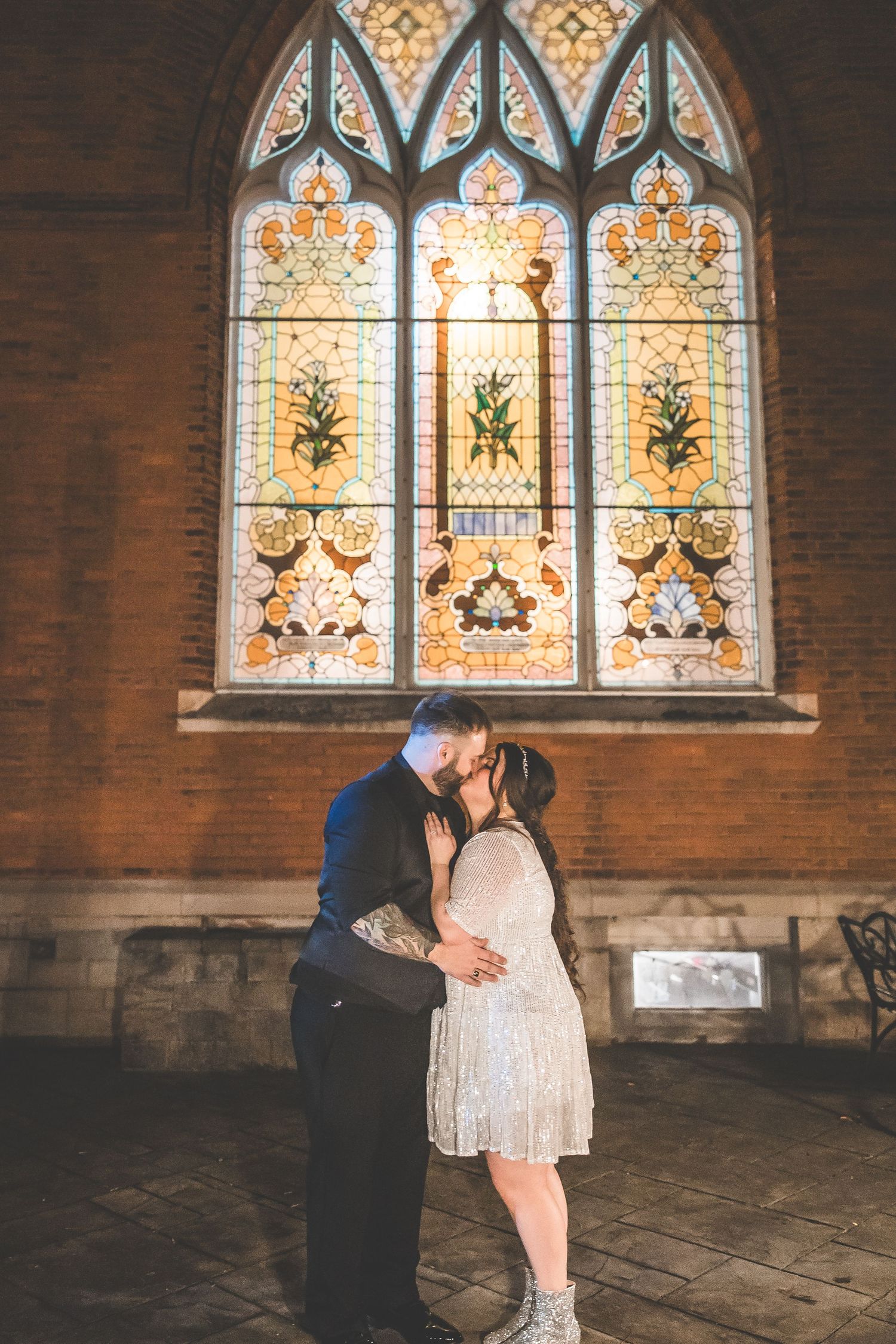 Couple sharing a romantic moment in front of ornate stained glass church windows.