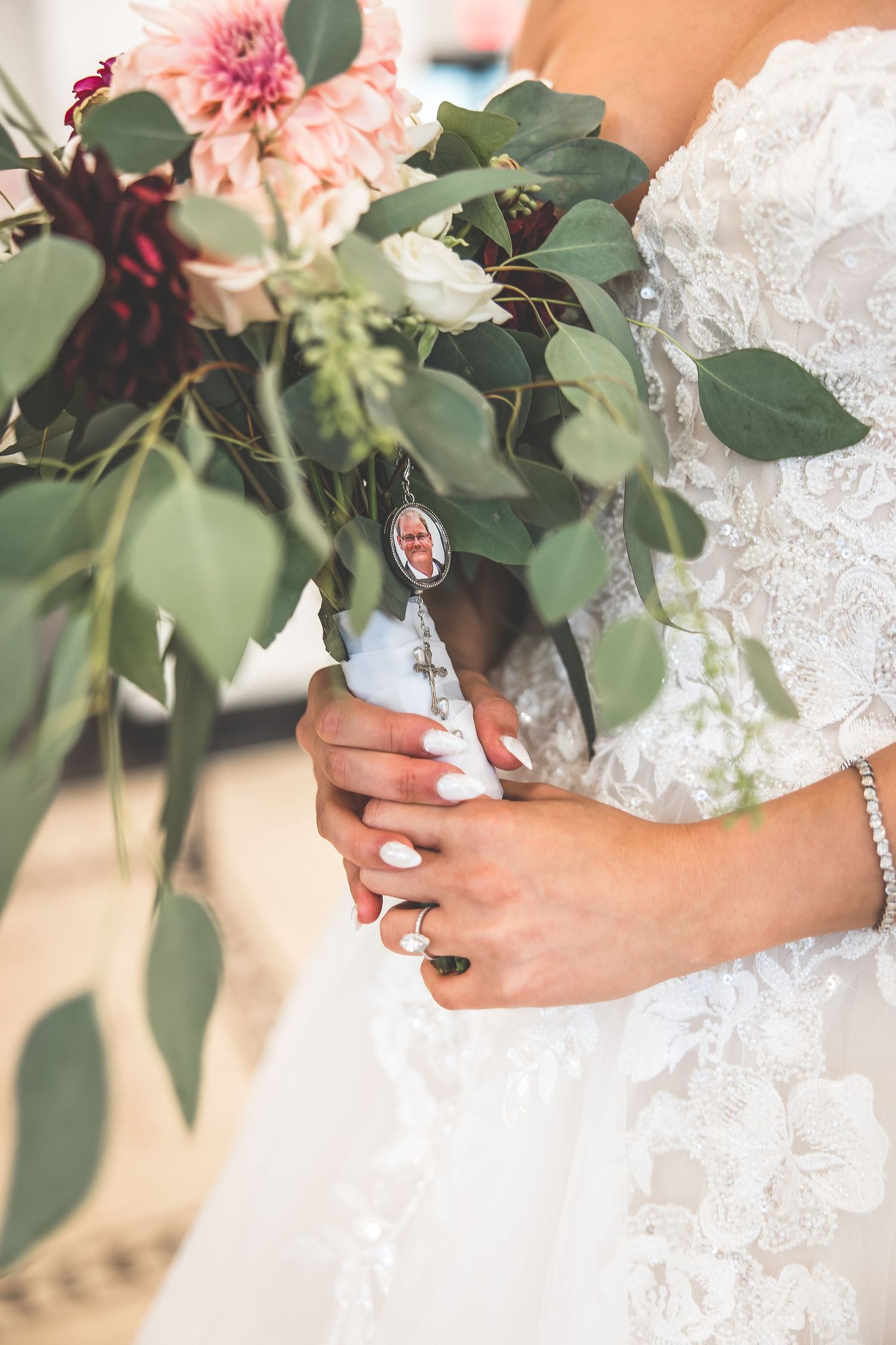 Close-up of bridal bouquet with pink flowers and greenery against white lace dress.