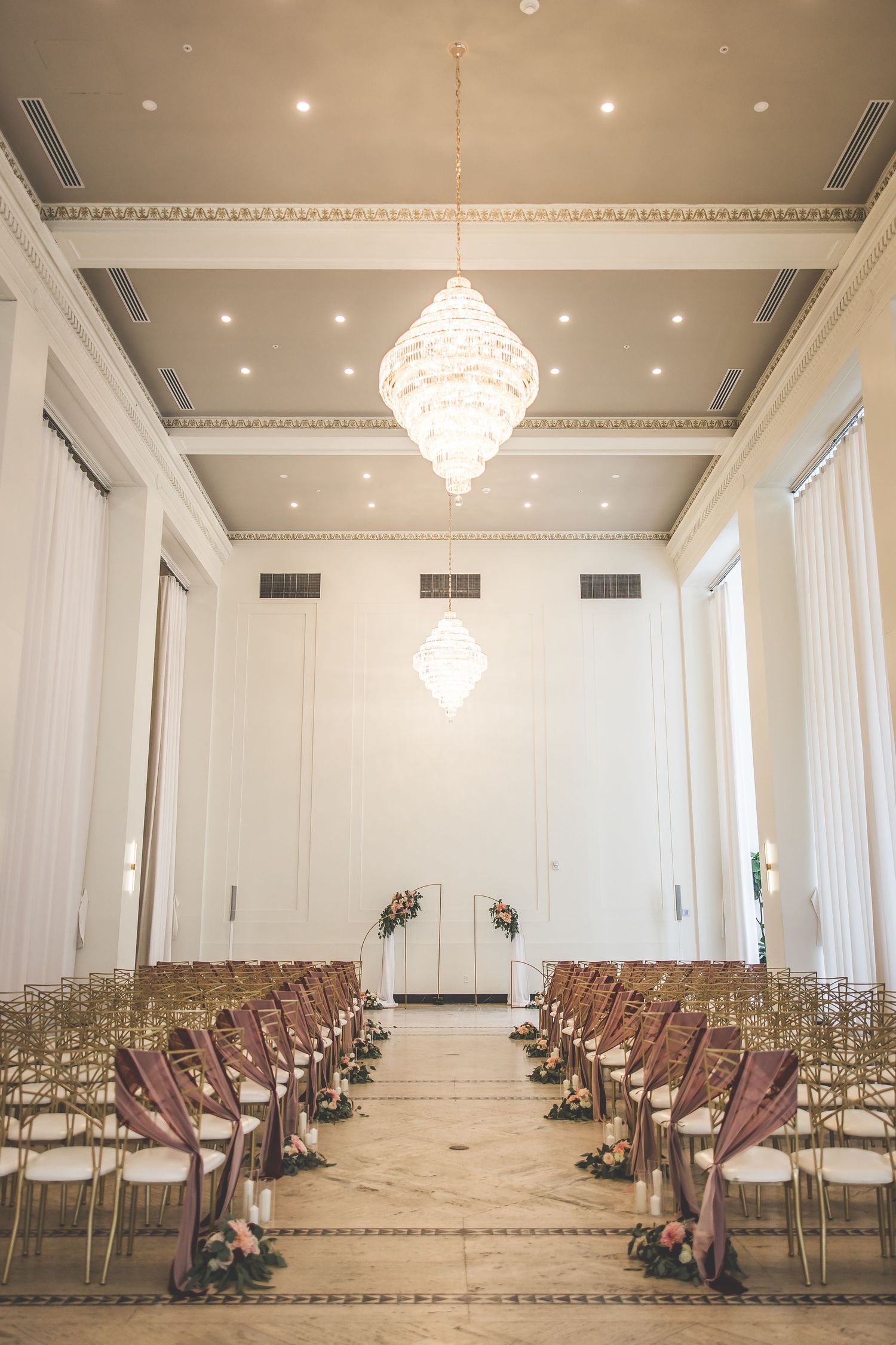 Wide view of an elegant wedding ceremony setup with rows of chairs and chandeliers.