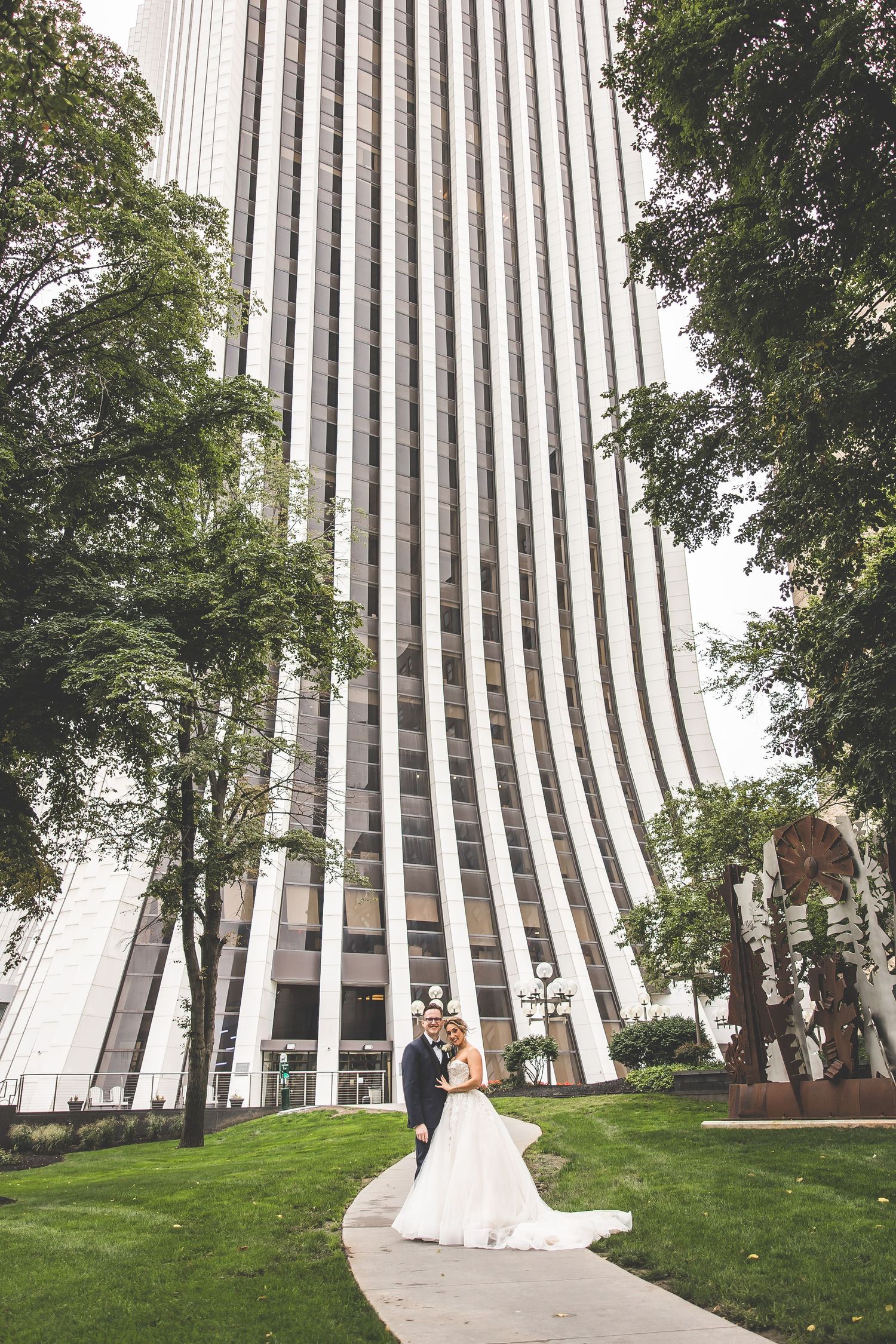 Wedding couple poses in front of a dramatic modern building with vertical stripes and green lawn.